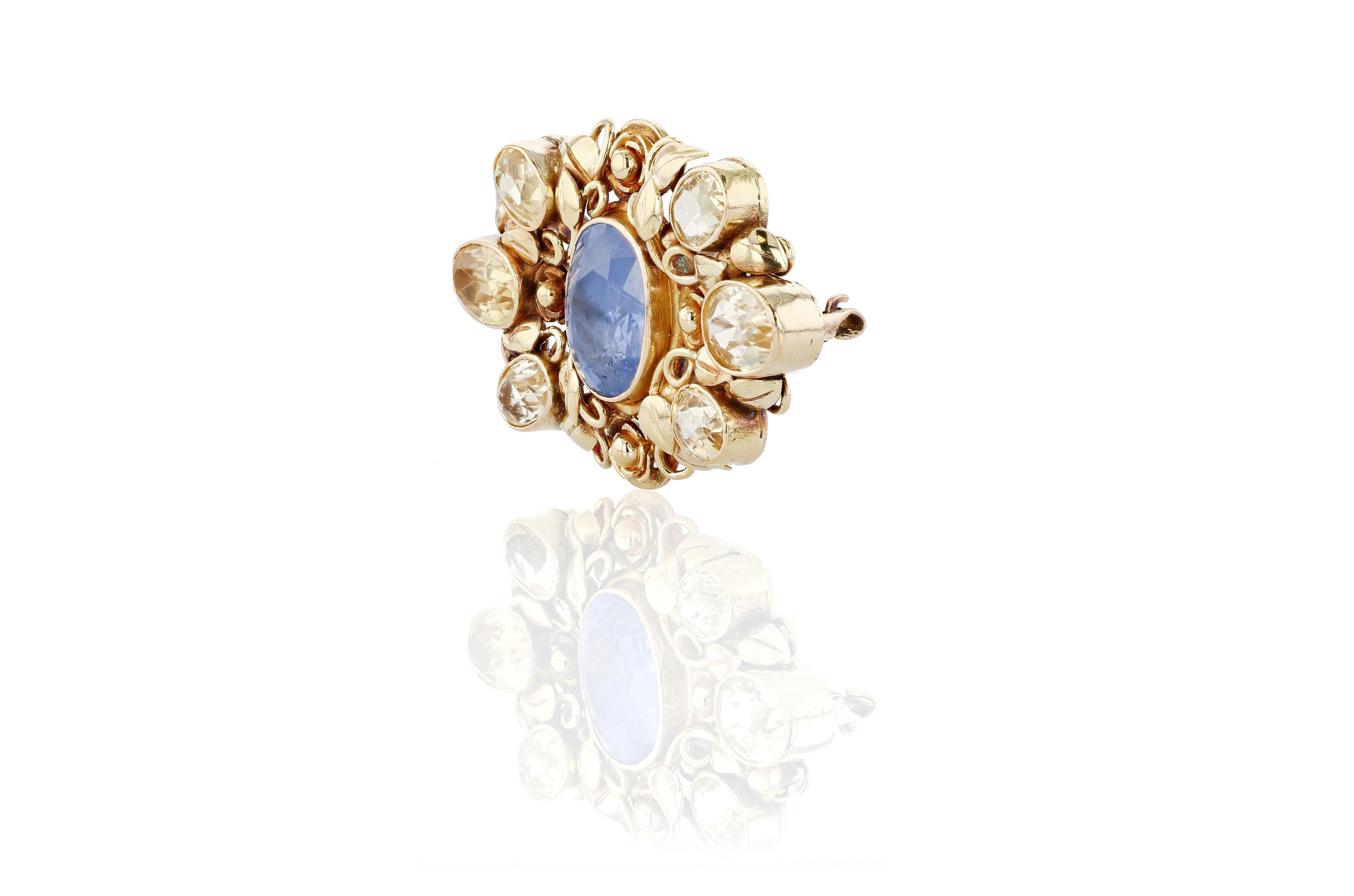A 1920s blue and yellow sapphire and citrine pin set in 22 karat yellow gold.

The pin centers a 2.50 carat blue sapphire, from which radiates five oval yellow sapphires and one light yellow citrine. Each stone, including the center stone, is bezel