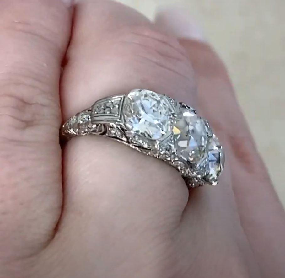 This exquisite Art Deco three-stone ring is a true testament to early 20th-century craftsmanship. At its heart lies a breathtaking antique cushion-cut diamond, weighing 2.22 carats, with a warm J color and SI2 clarity. Flanking this remarkable
