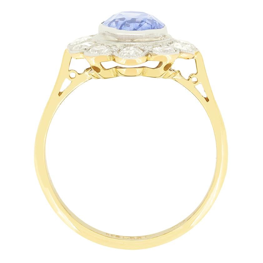 This stunning cluster ring dates back to the 1930s. At it’s heart sits an impressive 2.70 carat, cornflower blue sapphire. The sapphire is a natural stone cut in an oval shape and is rub over set into platinum. Enveloping the sapphire a ring of