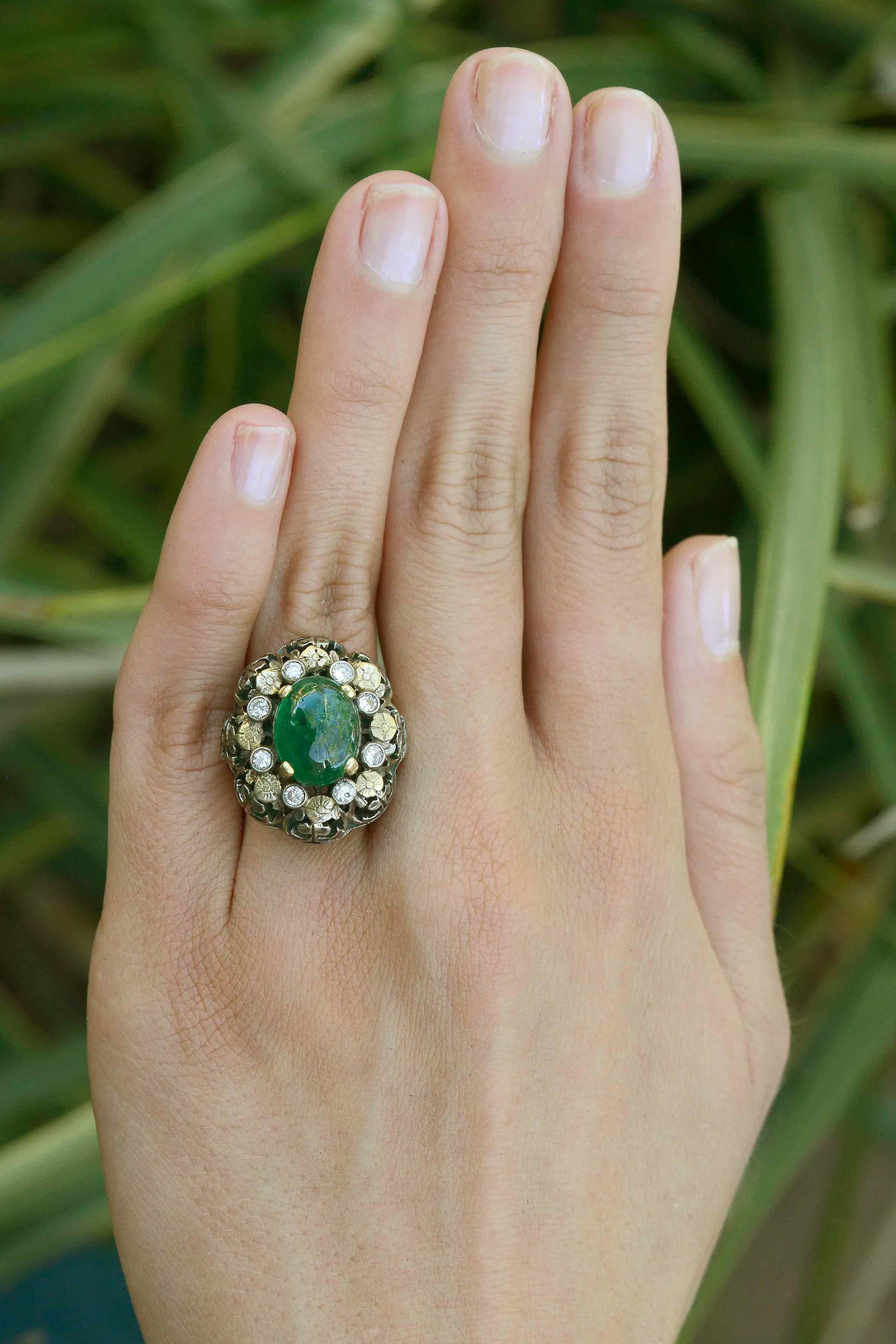 The Gilchrist antique 3 carat oval emerald cocktail ring is an exciting dome designed as a flower cluster. Centered by a natural Colombian emerald in cabochon, surrounded by sparkling brilliant diamonds and dotted with a floral motif. The 2 tone