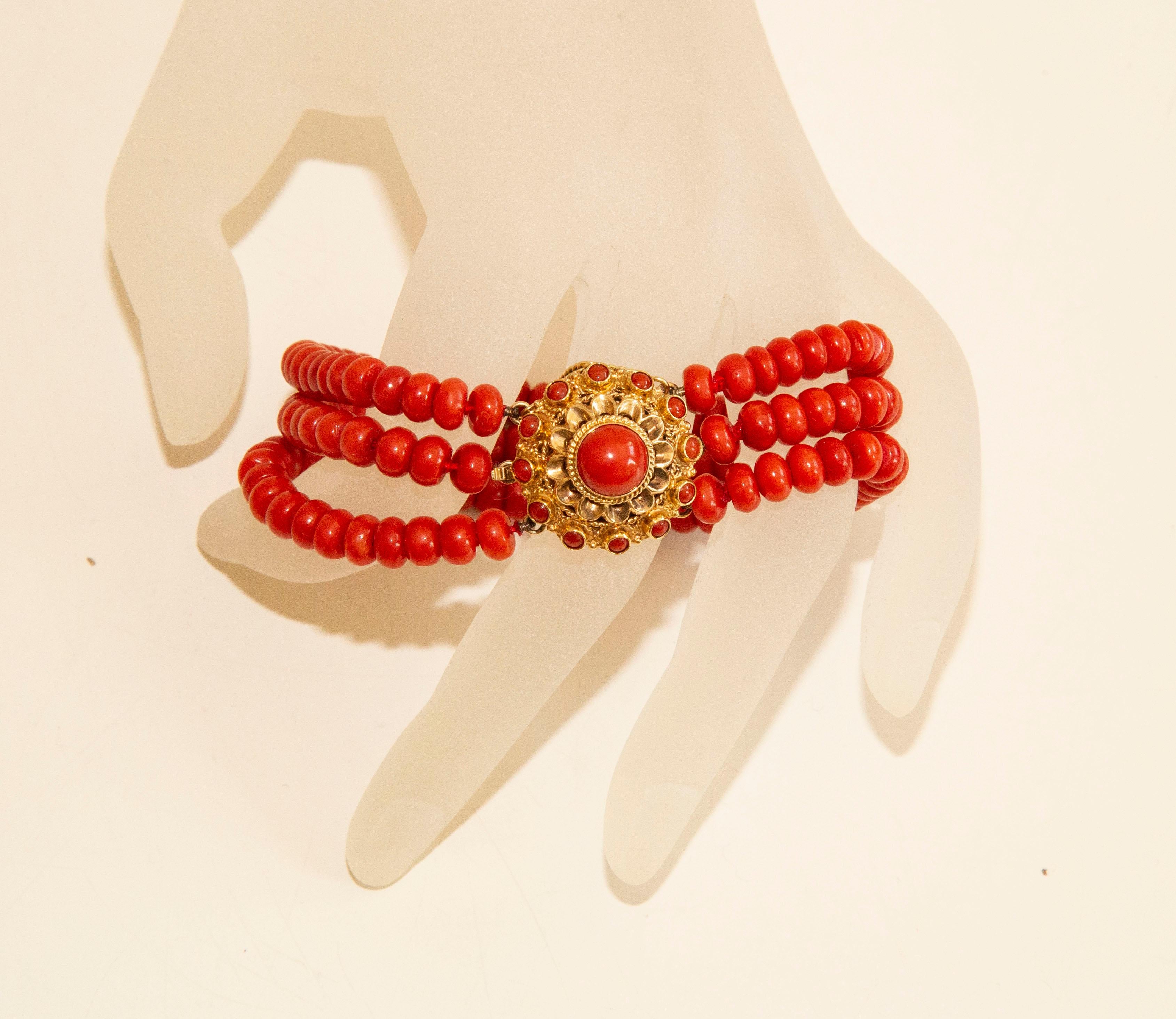 A vintage 3-row natural not dyed red coral bracelet with round filigree 14 karat yellow clasp with red coral cabochon in the centre and smaller beads on the periphery. The clasp features a 14k gold safety chain. The clasp is stamped with an oak leaf
