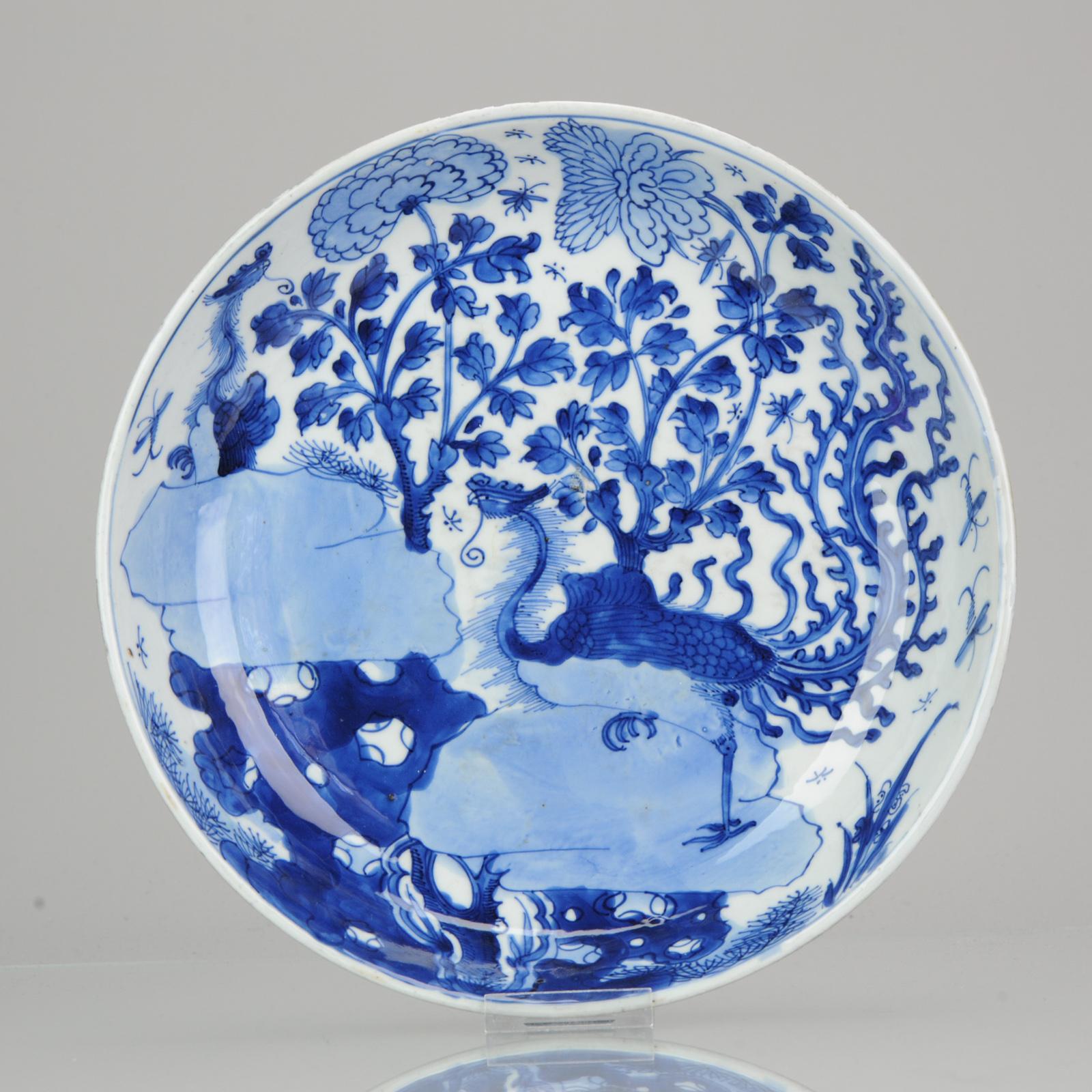 Large and very nice blue and white charger with a stunning landscape scene to get lost in. Central is a large Phoenix bird with beautiful large tail standing on a rock. Left above another phoenix is visible peaking over a rock. Further blossoming
