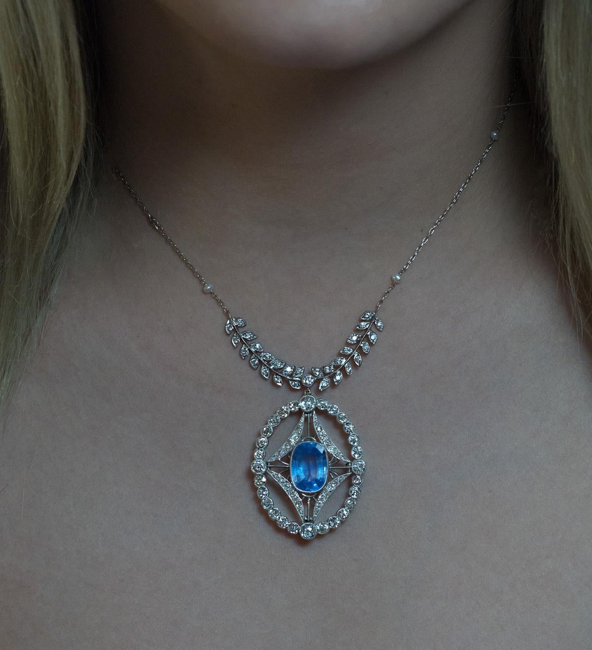 This platinum necklace consists of an oval openwork pendant, a chain with pearls, and a diamond garland. The pendant is circa 1910. It is handcrafted in platinum topped gold and centered with a sky blue Ceylon sapphire. The sapphire is surrounded by