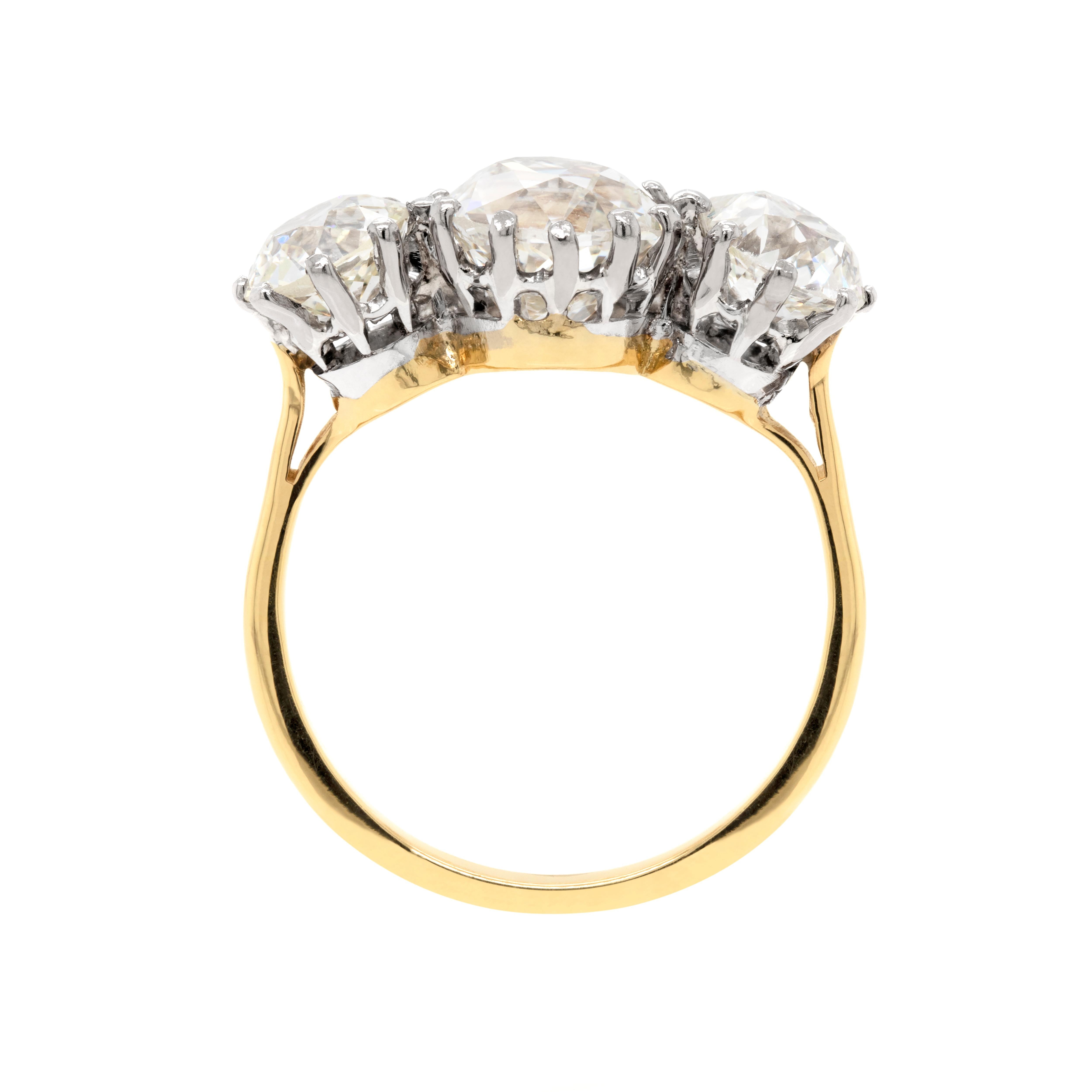 This exquisite 1920's three stone diamond engagement ring is timeless. The ring features a gorgeous cushion shaped Old Mine Cut diamond in the centre which weighs 2.50ct and is mounted in a 12 claw open back setting. The centre stone is beautifully
