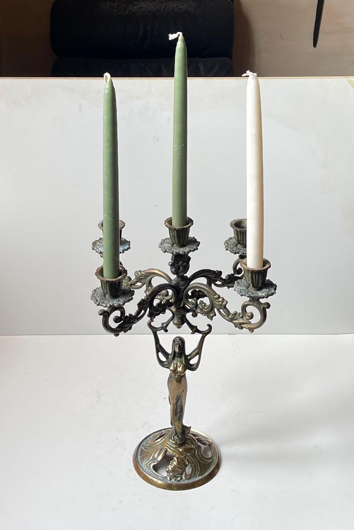 Magnificent candleholder in brass. Distinct early 20th century art nouveau - jugend styling. Female seductress with long hair/head scarf that transcends with her arms raising the tiered 5-arm candle configuration. It was made in Europe circa 1910-20