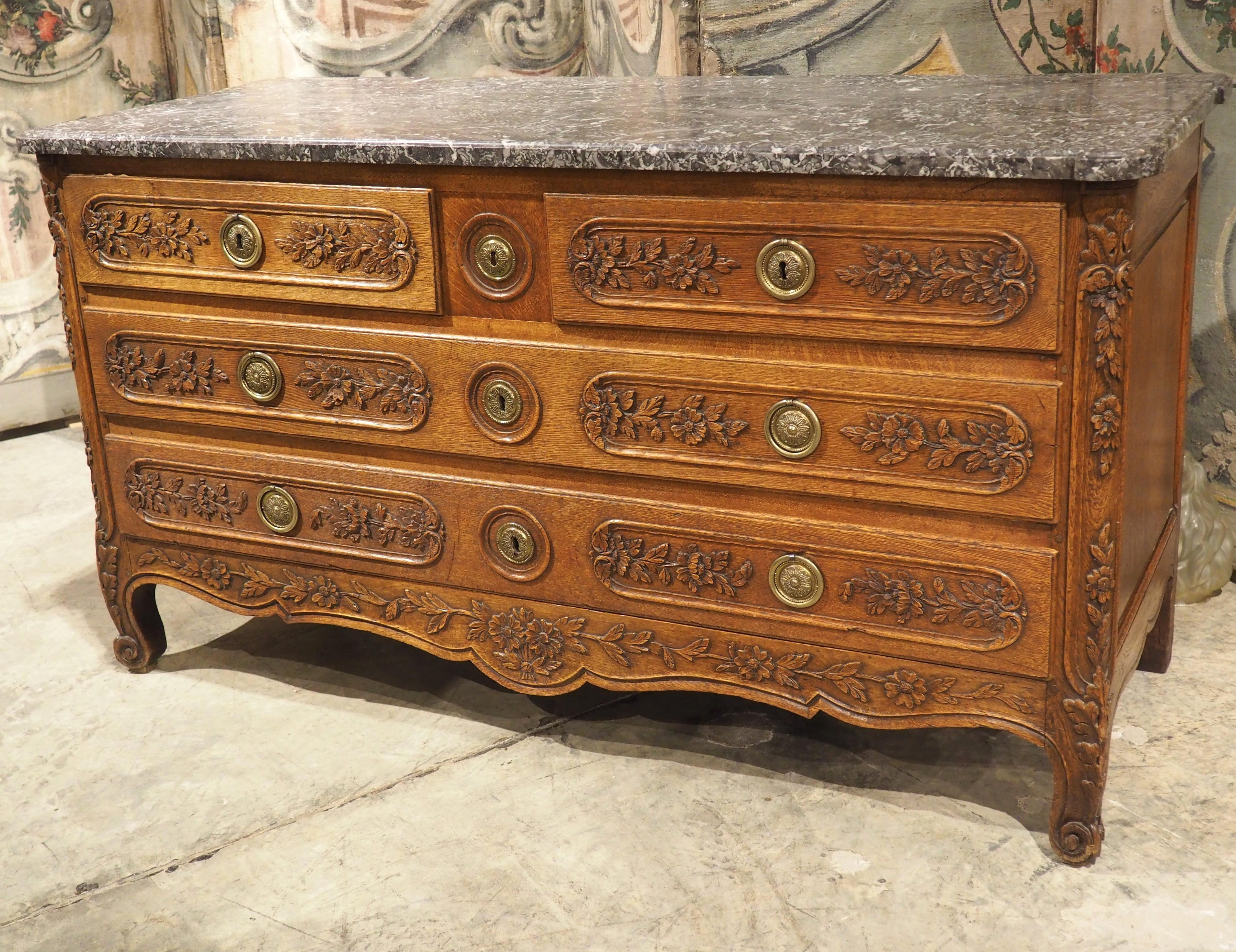 A rather unusual French commode, given the approximate width of 60 inches, this sculpted oak chest of drawers was hand-carved circa 1860. A relatively thin (1 1/8 inch in depth) original marble top enhances the elongated appearance by gently