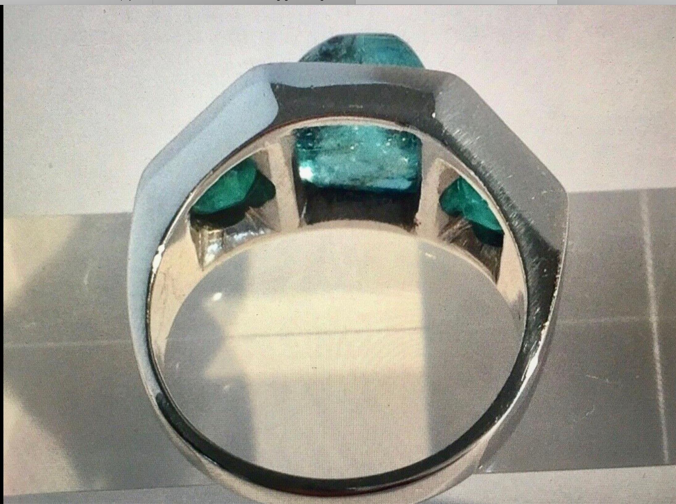 This stunning antique ring holds a natural Colombian emerald cabochon cut (with natural inclusions) weighing 3.00 carat, bezel set accented on each side with a  natural emerald round faceted cut weighing 2.00 carat, made of solid platinum.
Size 7