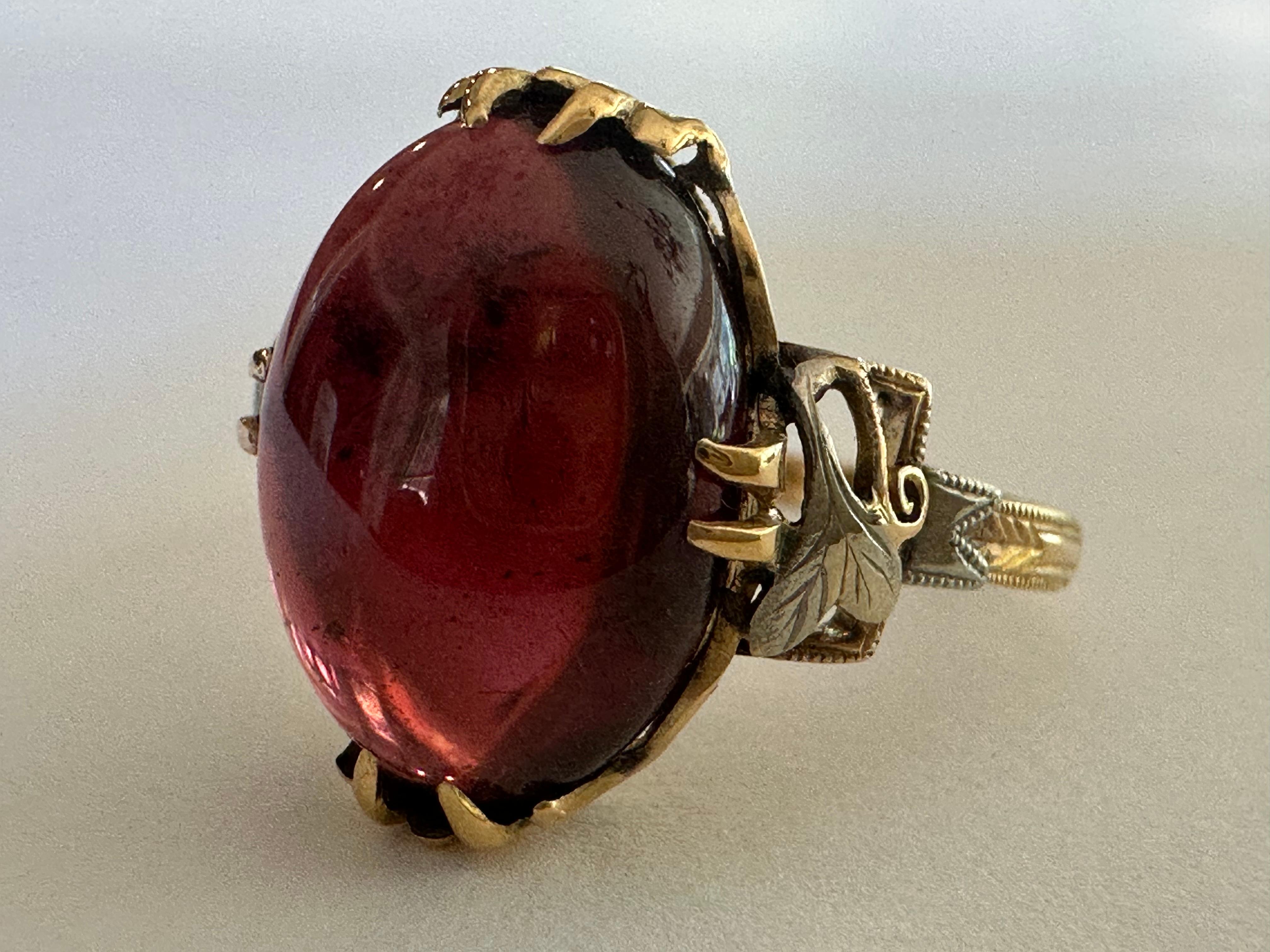 Cette bague dôme ancienne, probablement de la fin de l'ère victorienne, présente un grenat cabochon rouge vin de Tanzanie mesurant environ 14 X 10 mm et totalisant environ 7,63 carats. Serti en or jaune 18 carats avec des accents de feuilles d'or