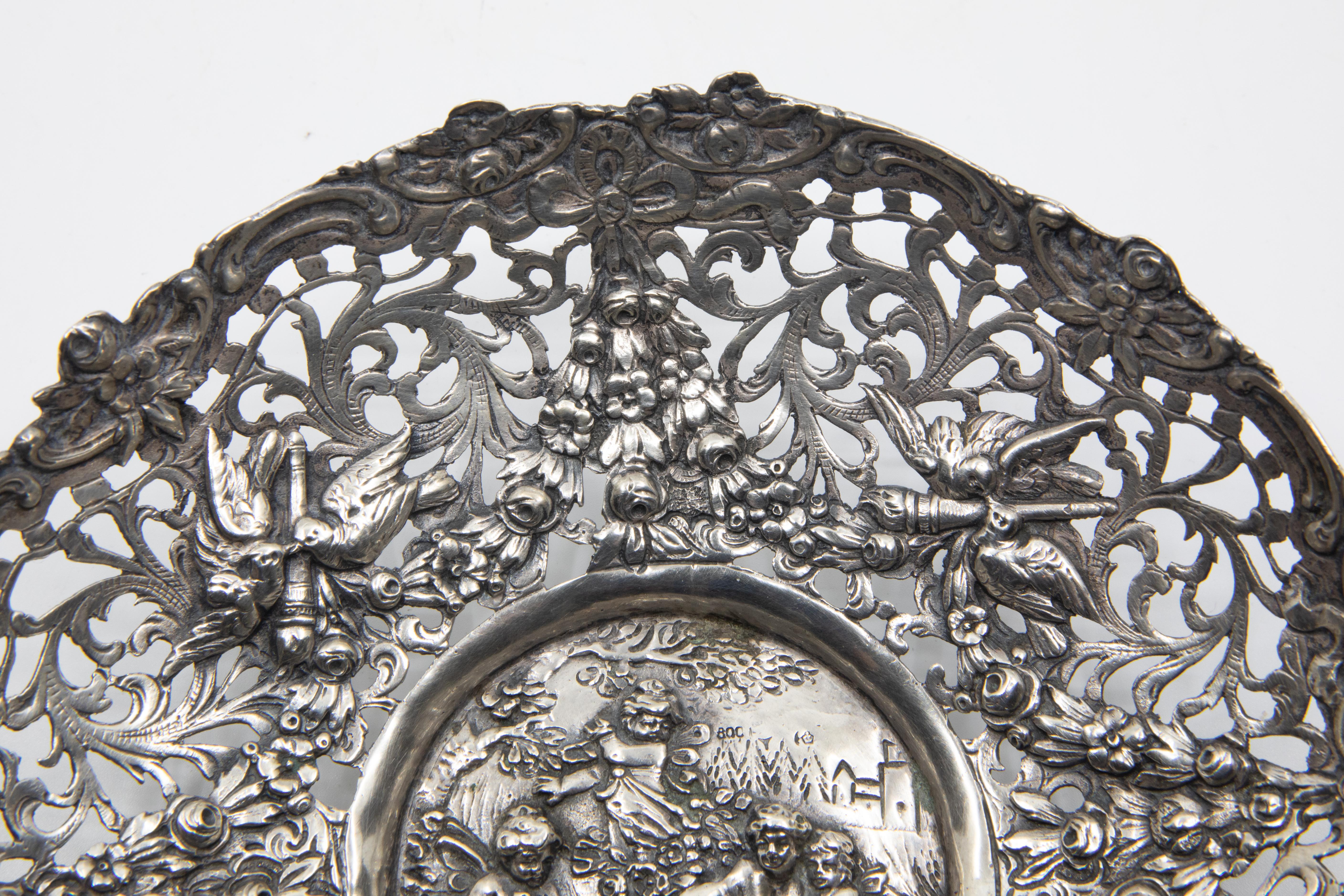 Antique 800 German silver repoussed dish. The dish has a Baroque design depicting frolicking cupids and doves with floral motifs.