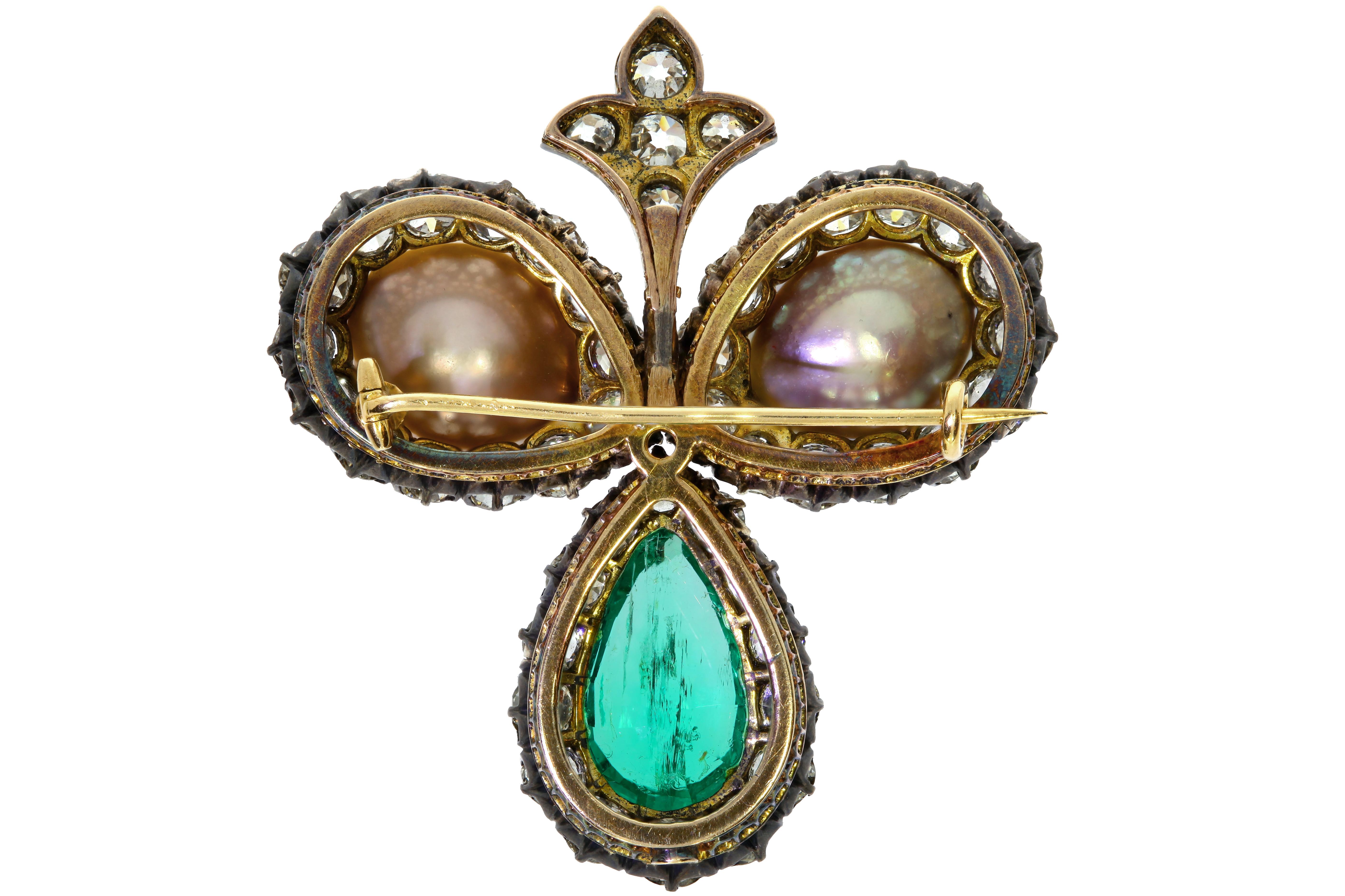 This Vintage brooch features two drilled pearls in a white and yellow metal brooch set with one 8.25 carats transparent, green, pear shaped emerald. Consists of one light gray natural and one cream colored pearl, as well as numerous transparent near