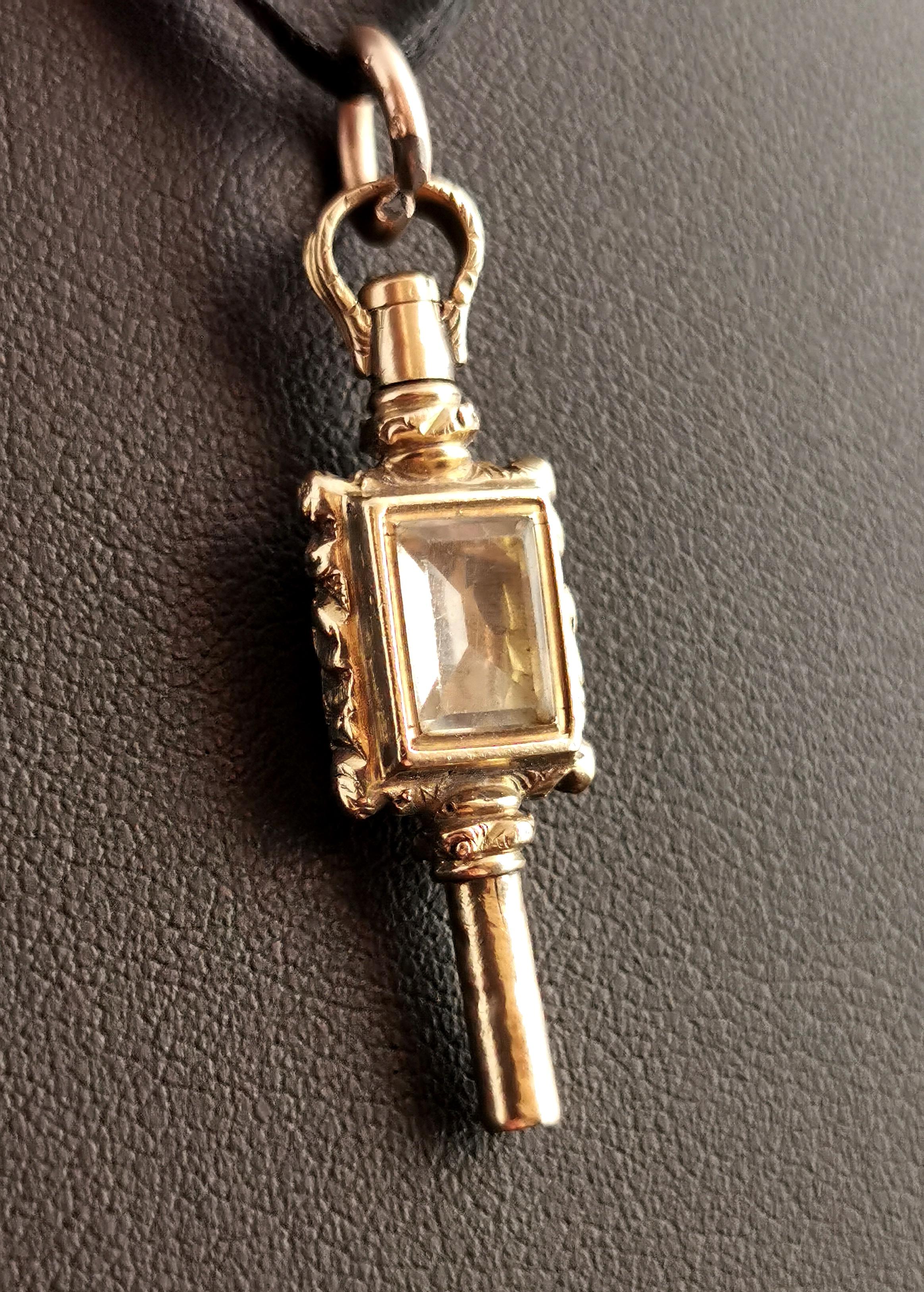 A charming little antique early Victorian era 9kt gold cased watch key pendant.

The key is cased in chased and engraved 9kt yellow gold with rectangular paste stone set to each side.

On one side a light yellow faux citrine and the other an opaque