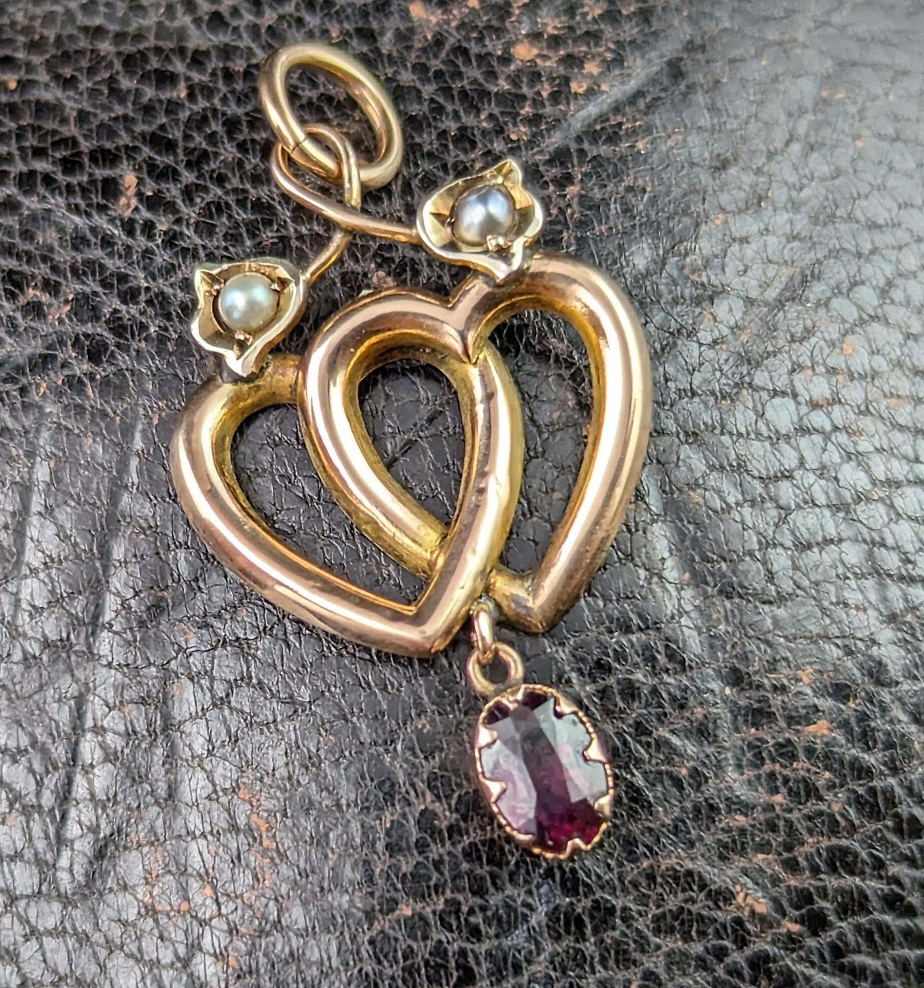The sweetest little antique double heart dropper pendant.

Crafted in 9ct gold with rosey tones it features double entwined hearts each with a pretty tulip flower to the top twirling around the curve of the heart and set with a tiny seed pearl.

The