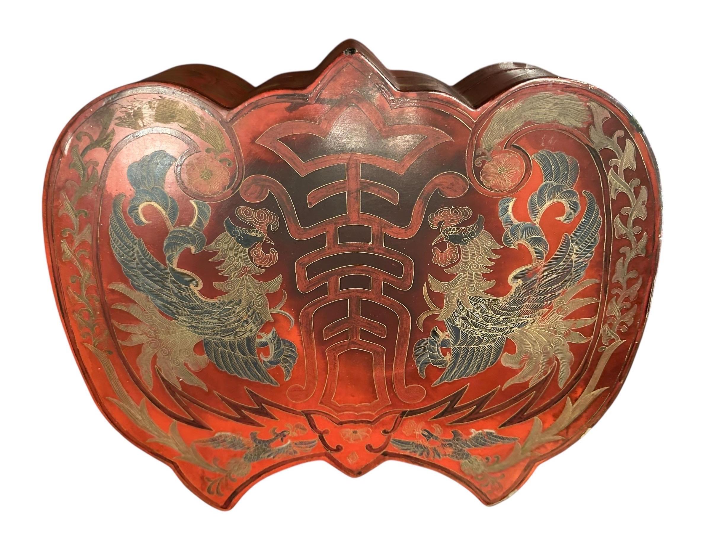Ancienne boîte en laque rouge chinoise de forme rare, probablement du début du 20e siècle, présentant des décorations symboliques.  Il est fabriqué en bois laqué, un artisanat traditionnel chinois.
La boîte est rouge avec des détails dorés et noirs,