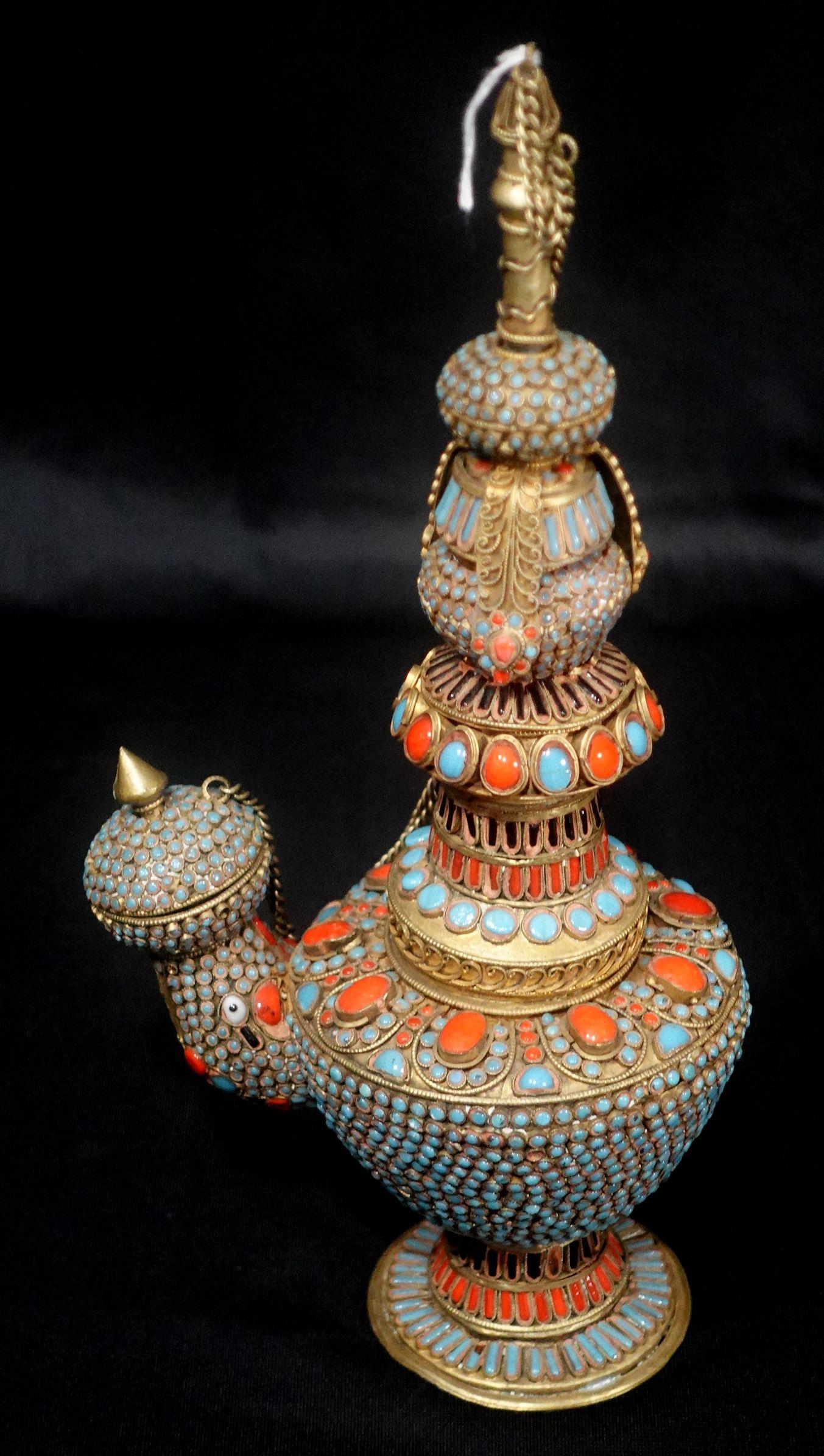 A Tibetan handmade pot with the spout being a head with wire work and mounted jewelry stones overall. It can be disassembled in pieces and put back together again.
12 1/2 inches High.