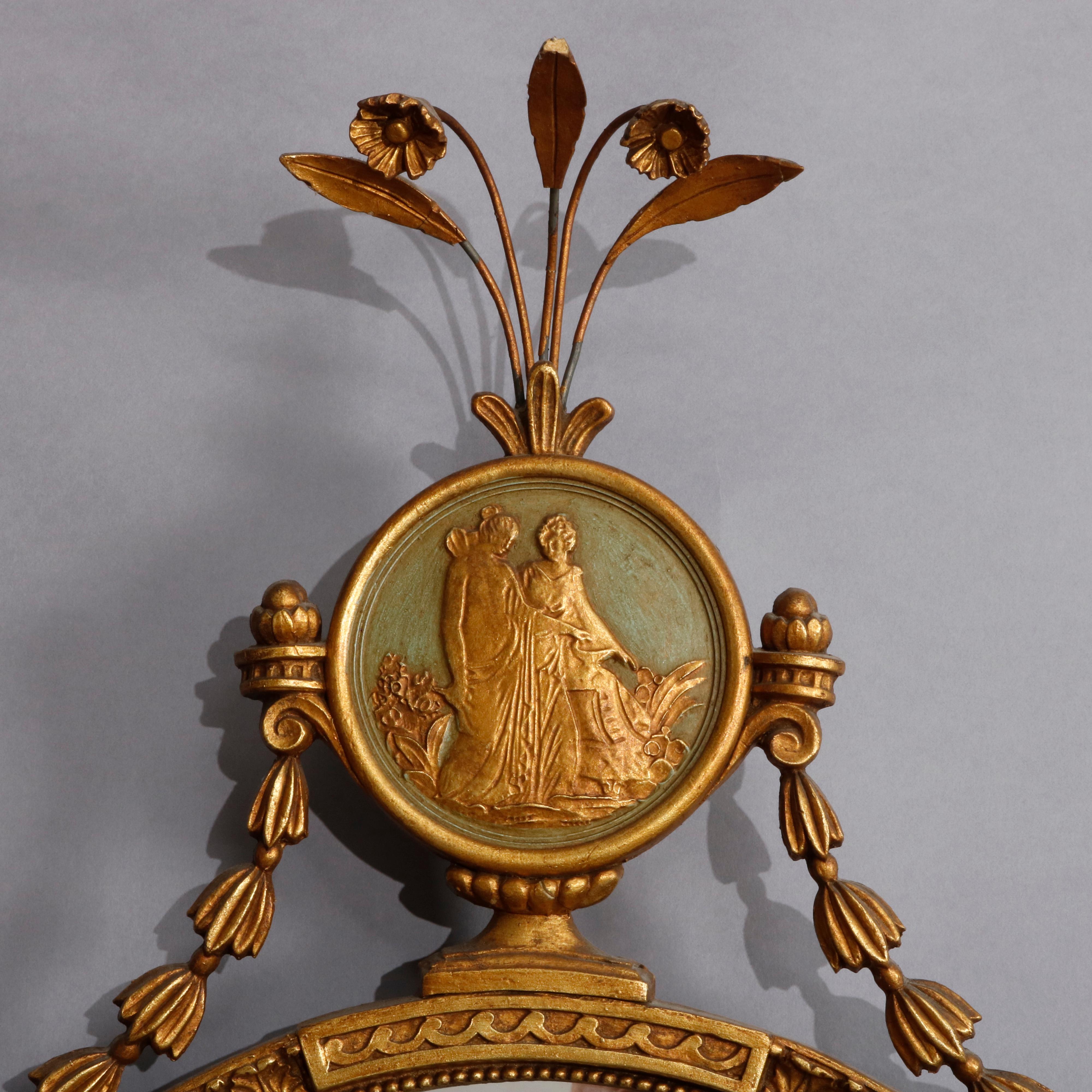 An antique Adam style wall mirror features foliate crest surmounting polychromed medallion with classical scene and oval mirror having flanking bellflower drape, circa 1919

Measures: 43.75