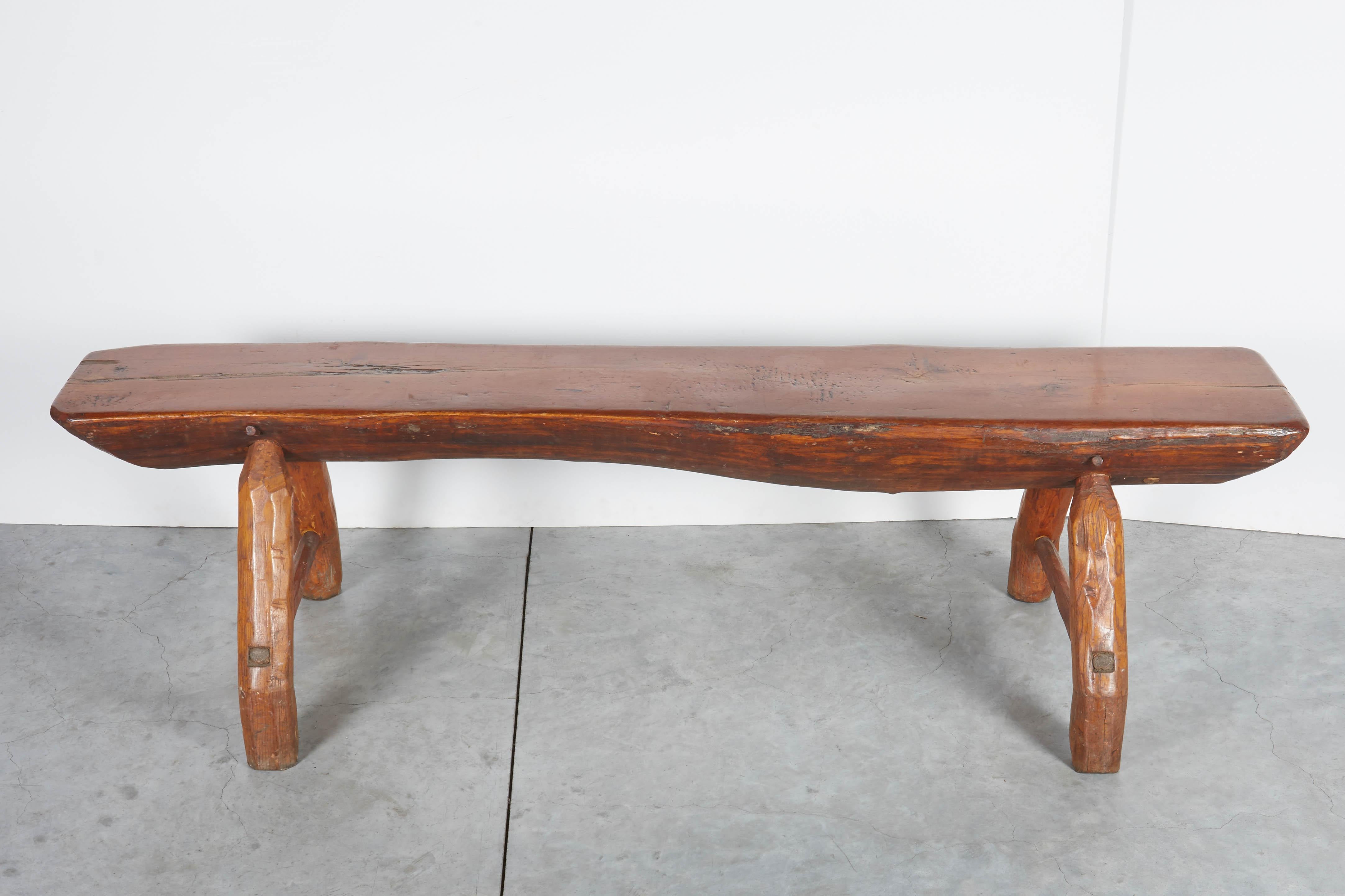 A very striking antique adirondack bench with a gracefully shaped thick seat formed out of a single piece of wood. The remarkable seat is supported by two unique hand carved legs that give this bench it's remarkable  character. 
Dimensions: seat:
