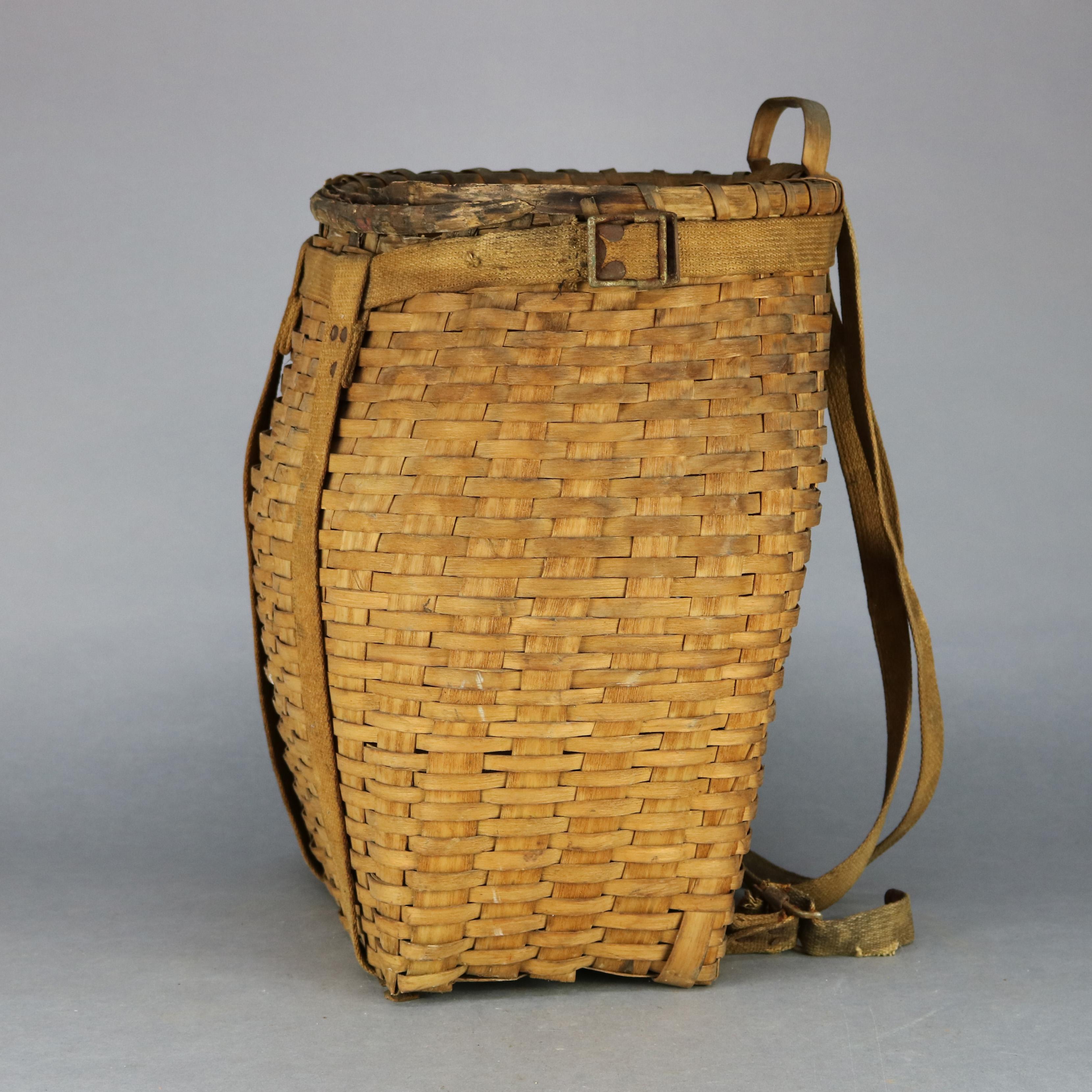 An antique Adirondack pack basket offers molded reed frame with handle, woven ash basket and fabric strap and buckle harness, circa 1910.

Measures: 20