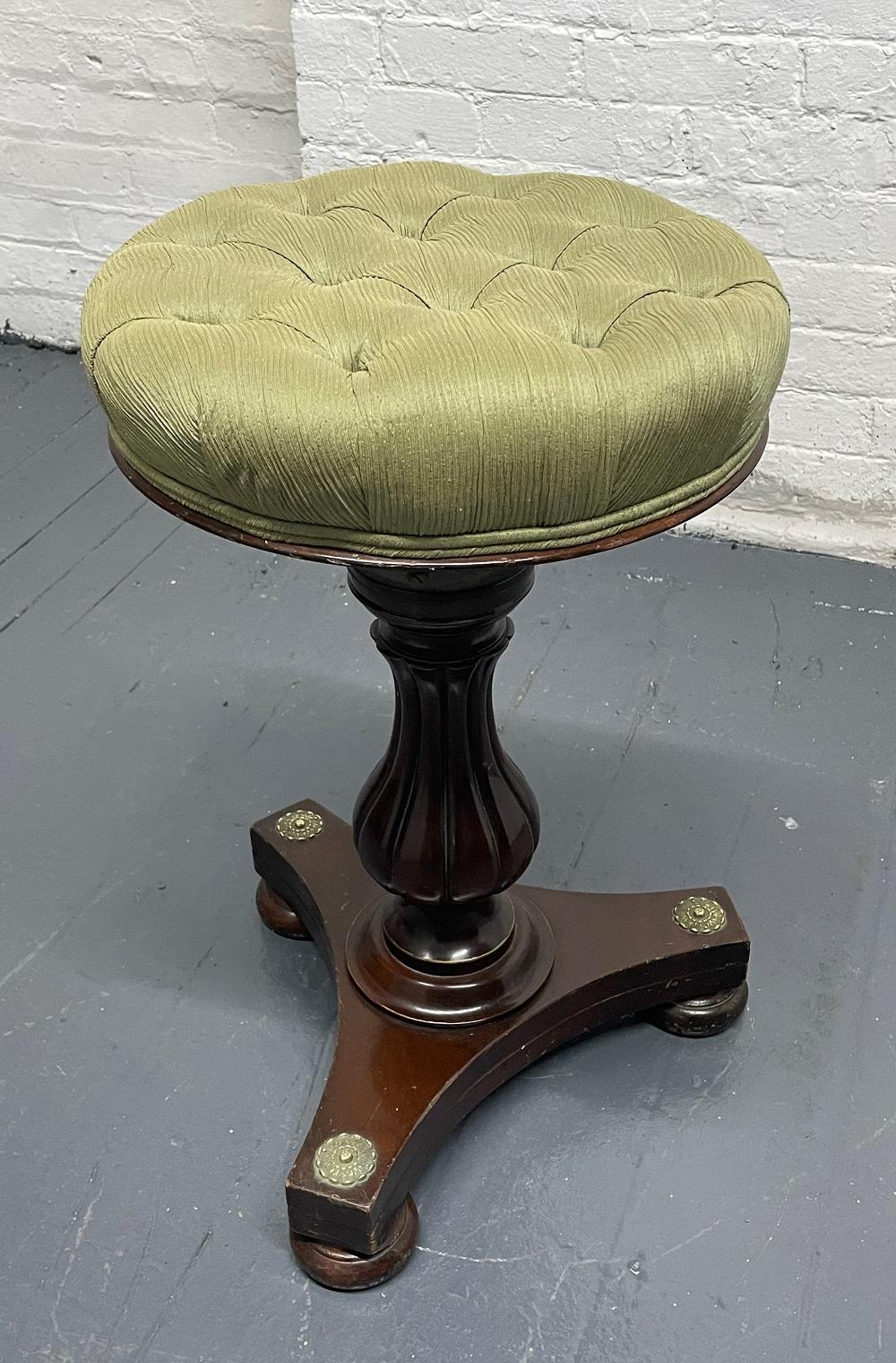 Antique adjustable mahogany and brass stool. The stool has a tufted seat with brass accents to the frame.