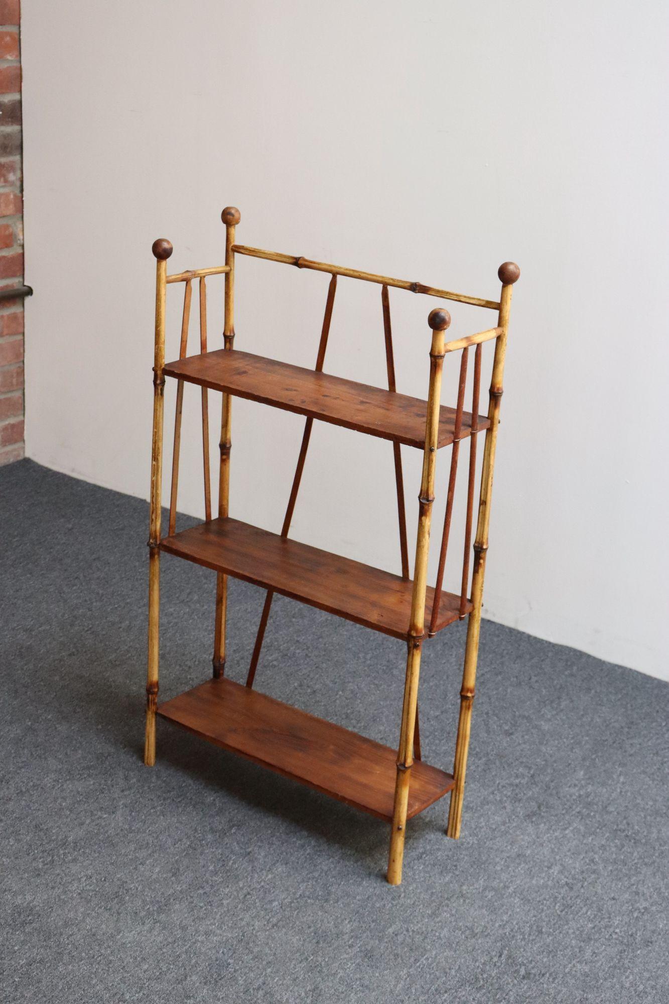 Antiguo etagere/librero/estantería de tres niveles (ca. principios del siglo XX, EEUU).
Compuesto por un armazón de bambú con herrajes metálicos que sostiene tres estantes de nogal y adornado con remates redondos tallados a mano.
Estantería estrecha