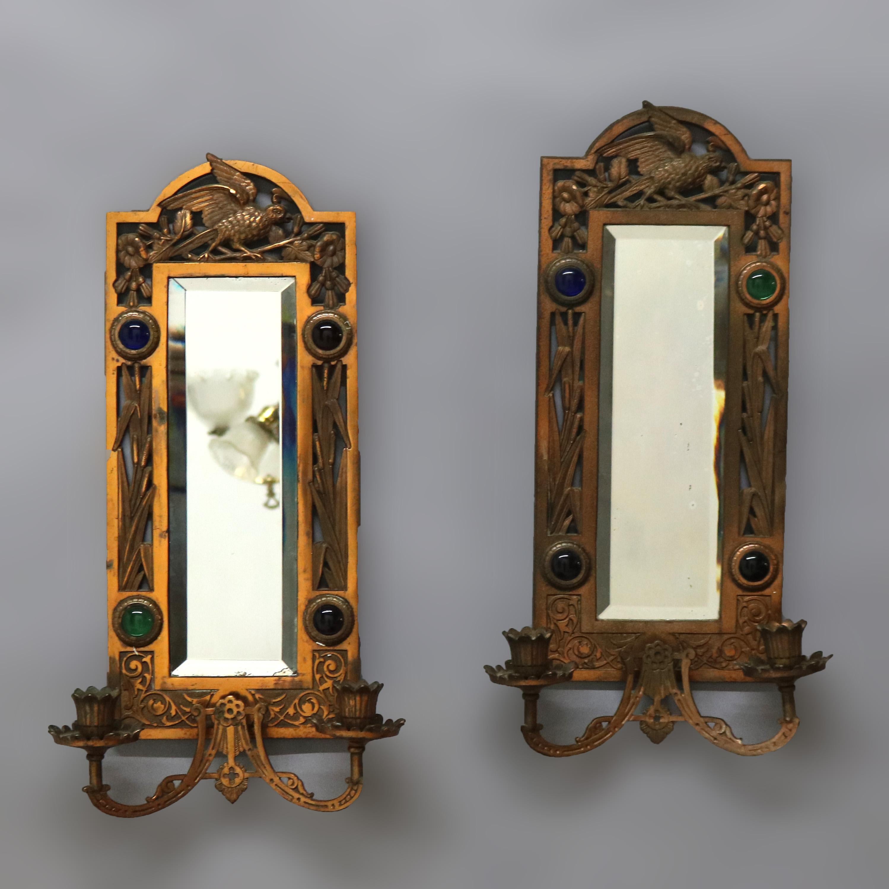 An antique pair of Aesthetic Movement mirrored wall sconces offer bronzed cast metal frames with a bird form pediments, marsh elements and double arms terminating in candle sockets; jeweled highlights throughout; c1880

Measures - 20