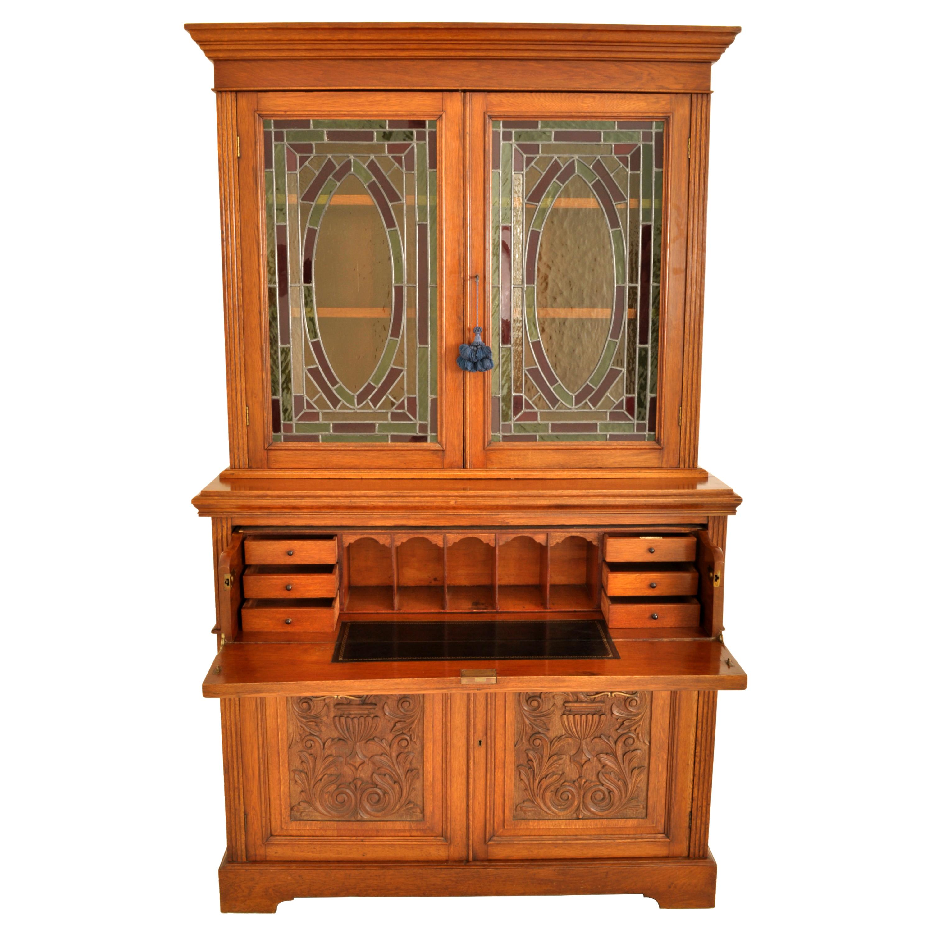 A good English Aesthetic Movement carved ash and leaded/stained glass secretary bookacse, circa 1890.
The bookcase desk in two parts, the top with a stepped cornice, below is a pair of doors with colored leaded glass panels with a central oval