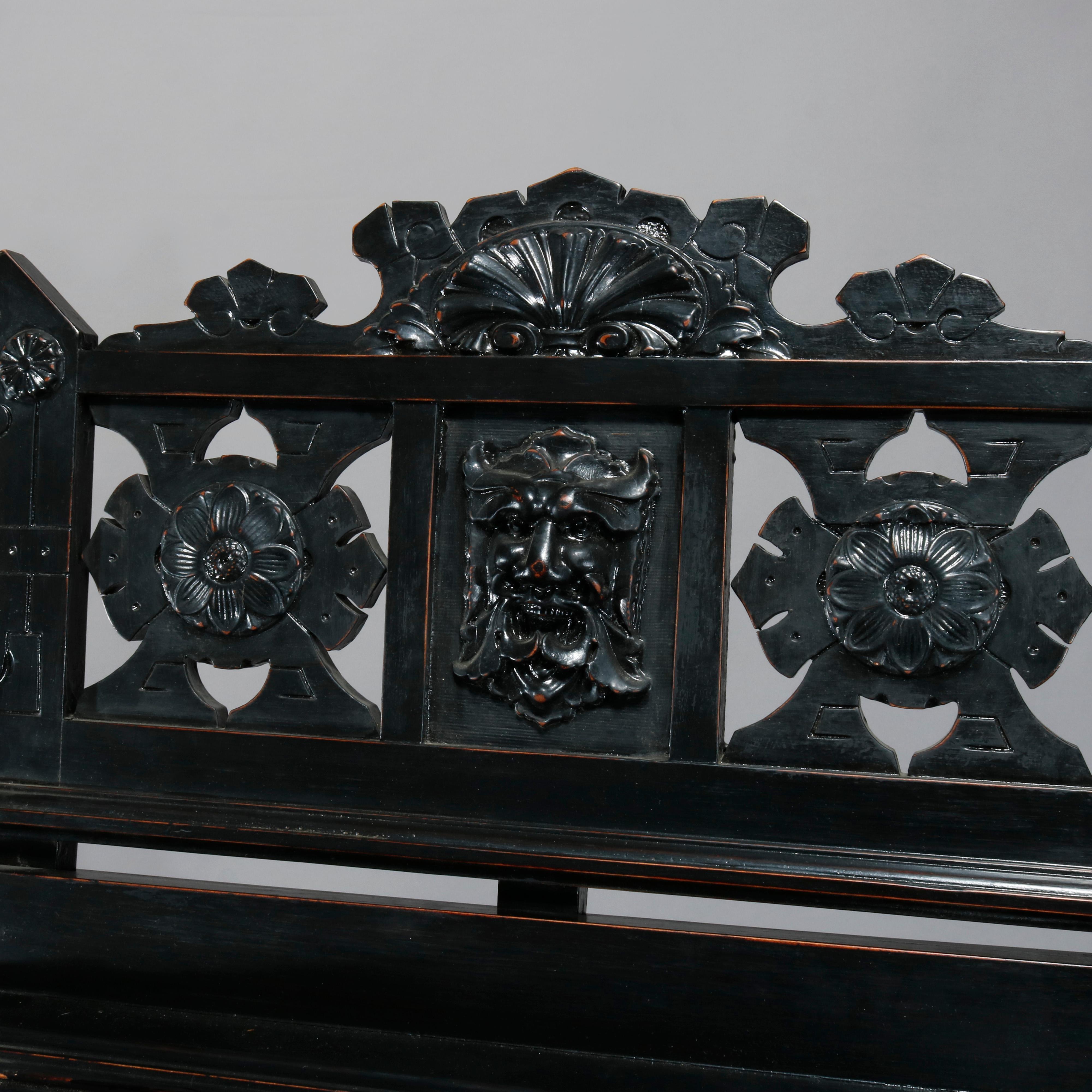 An antique Aesthetic Movement portfolio stand offers ebonized wood construction with carved and pierced crest having central mask with flanking floral and foliate elements surmounting stand with fold-up panels having carved elements of musical