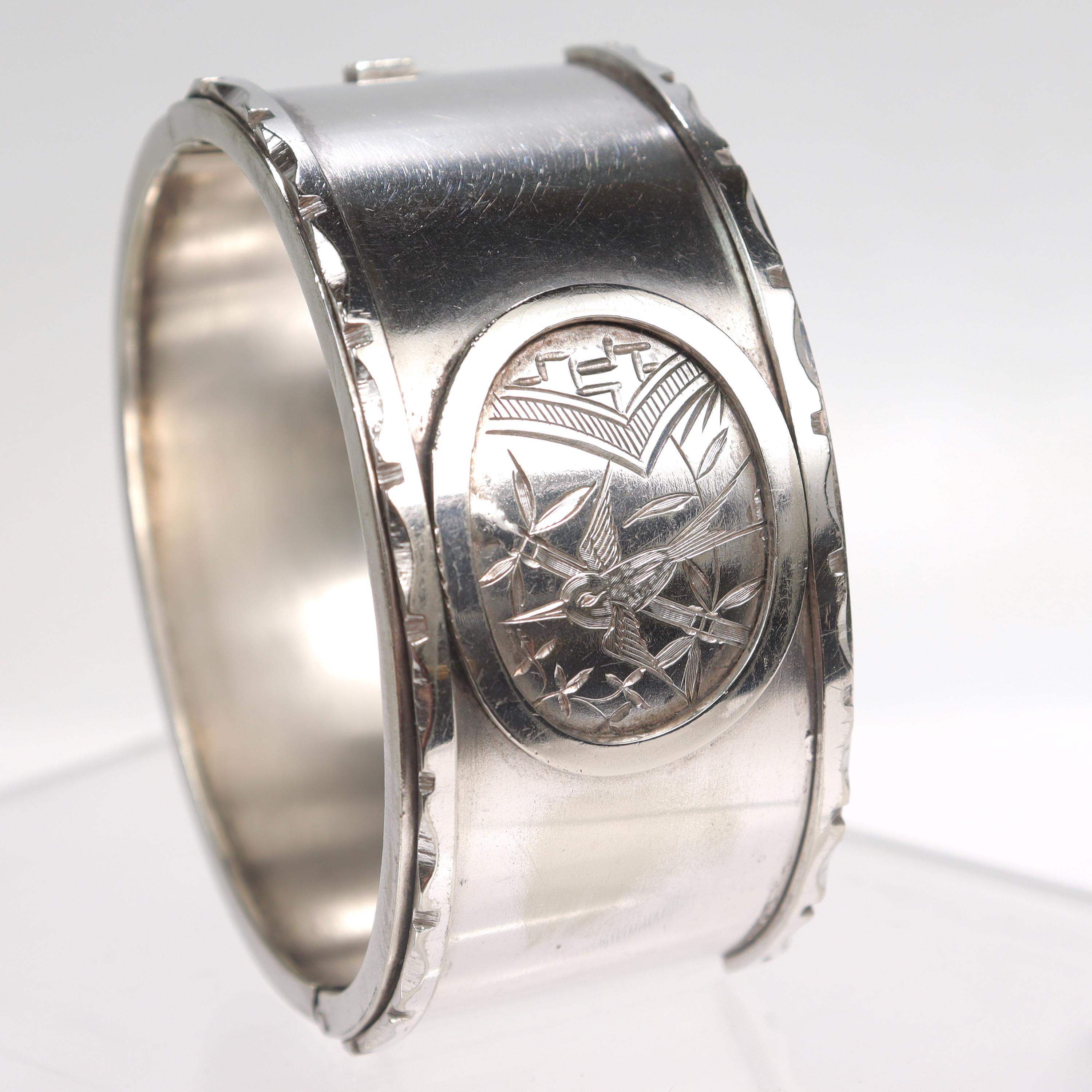 A fine, antique Aesthetic Period bangle bracelet.

In sterling silver.

With an engraved Japonismé pattern including a bird and leaves in a oval cartouche to the center of cuff. Each outside edge is finished with a repeating, notched pattern.

Opens