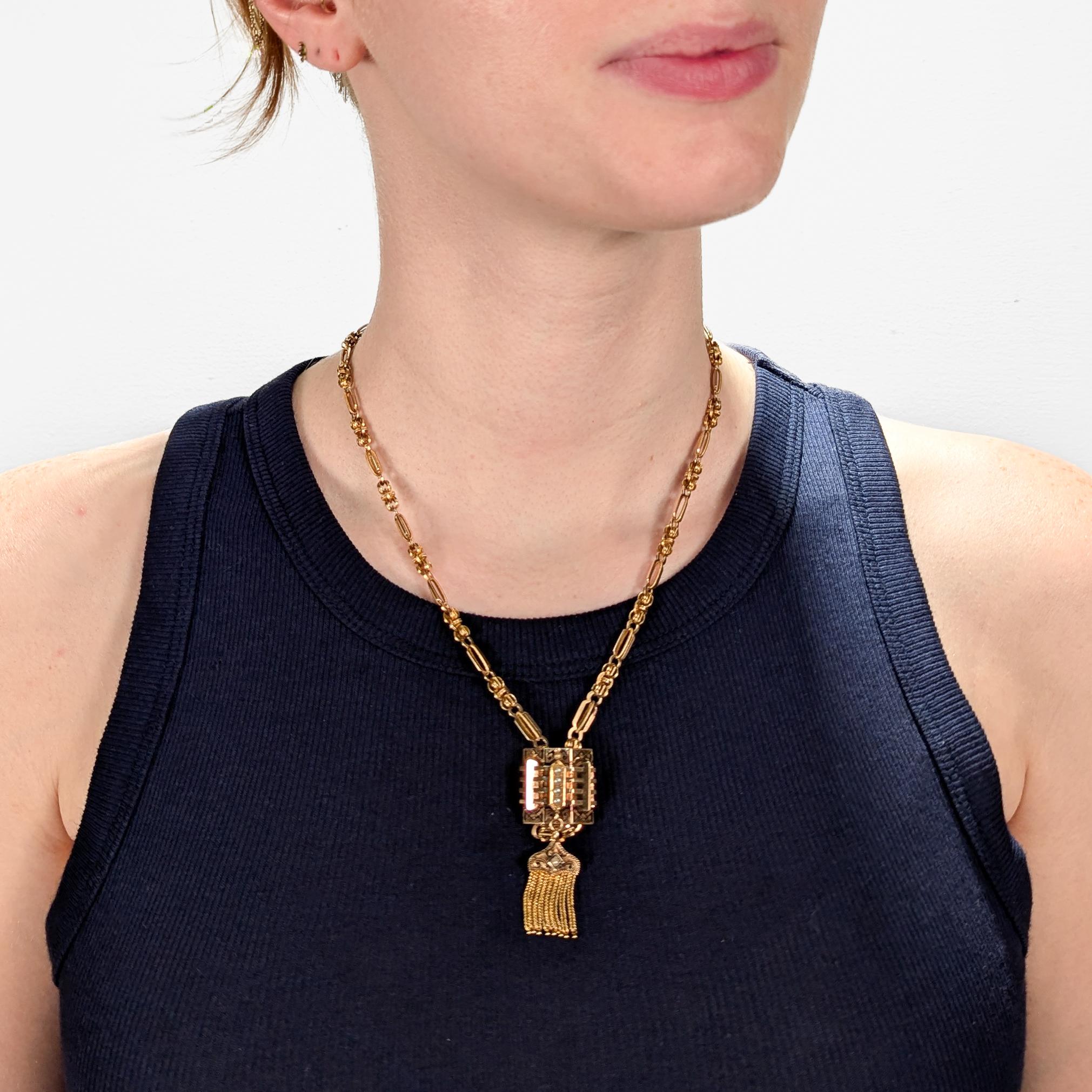 A fine antique Aesthetic Period slide necklace.

In 14 karat yellow gold.

With a complex chain link necklace supporting a geometric slide that has black enamel decoration, prong-set white pearls, and an attached tasseled drop. 

Simply a wonderful