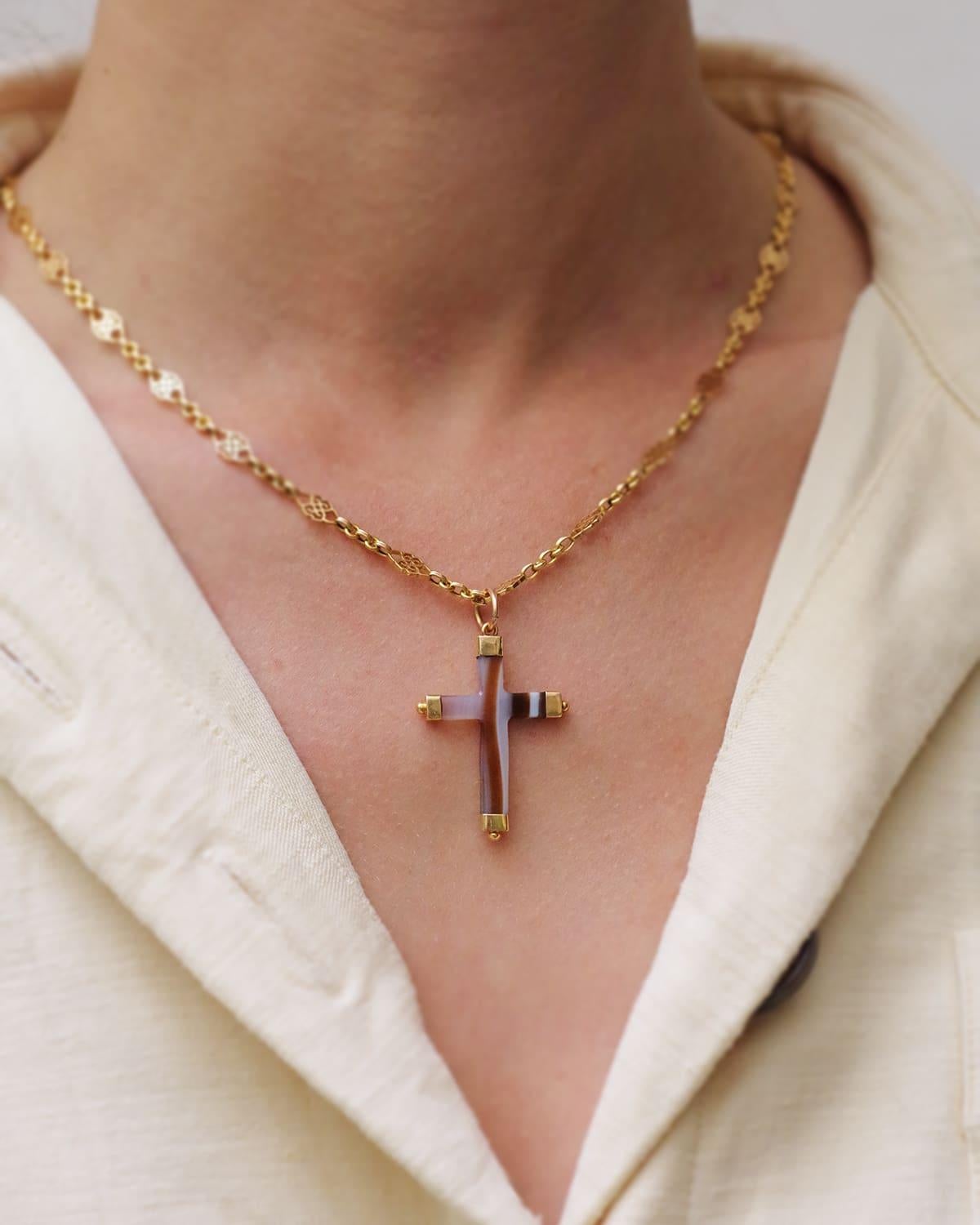 Antique agate cross pendant in 18 karat gold. Antique cross carved from a zoned agate with white, brown, and translucent white color, also called sardonyx. The ends are decorated with a gold setting decorated with spheres. The bail is made of 14