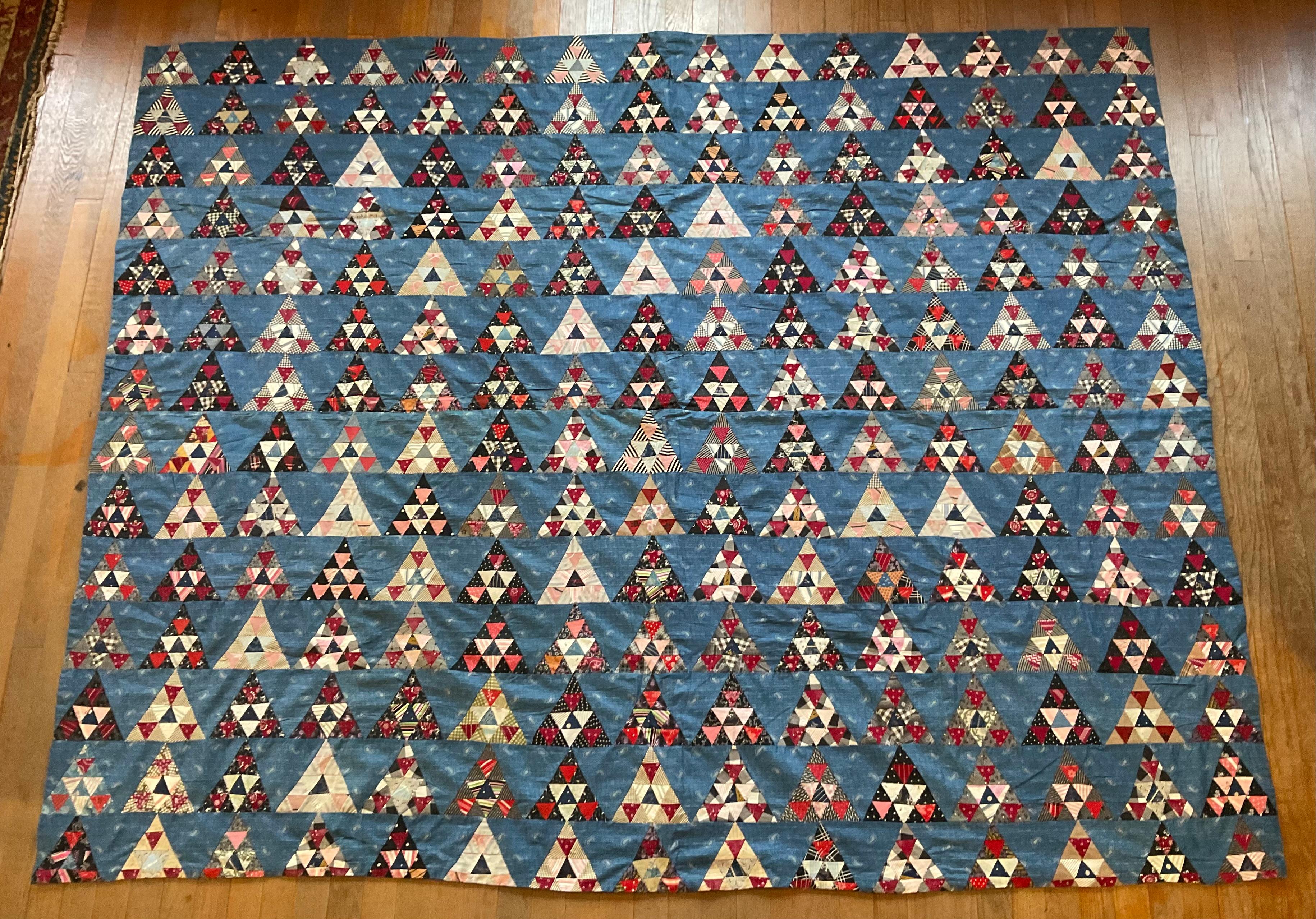 un'antica trapunta americana di grande formato, un vero pezzo di storia tessile e di arte popolare. Questa magnifica trapunta presenta un complesso e ipnotico motivo a triangolo a mosaico, meticolosamente cucito a mano da centinaia di singole pezze