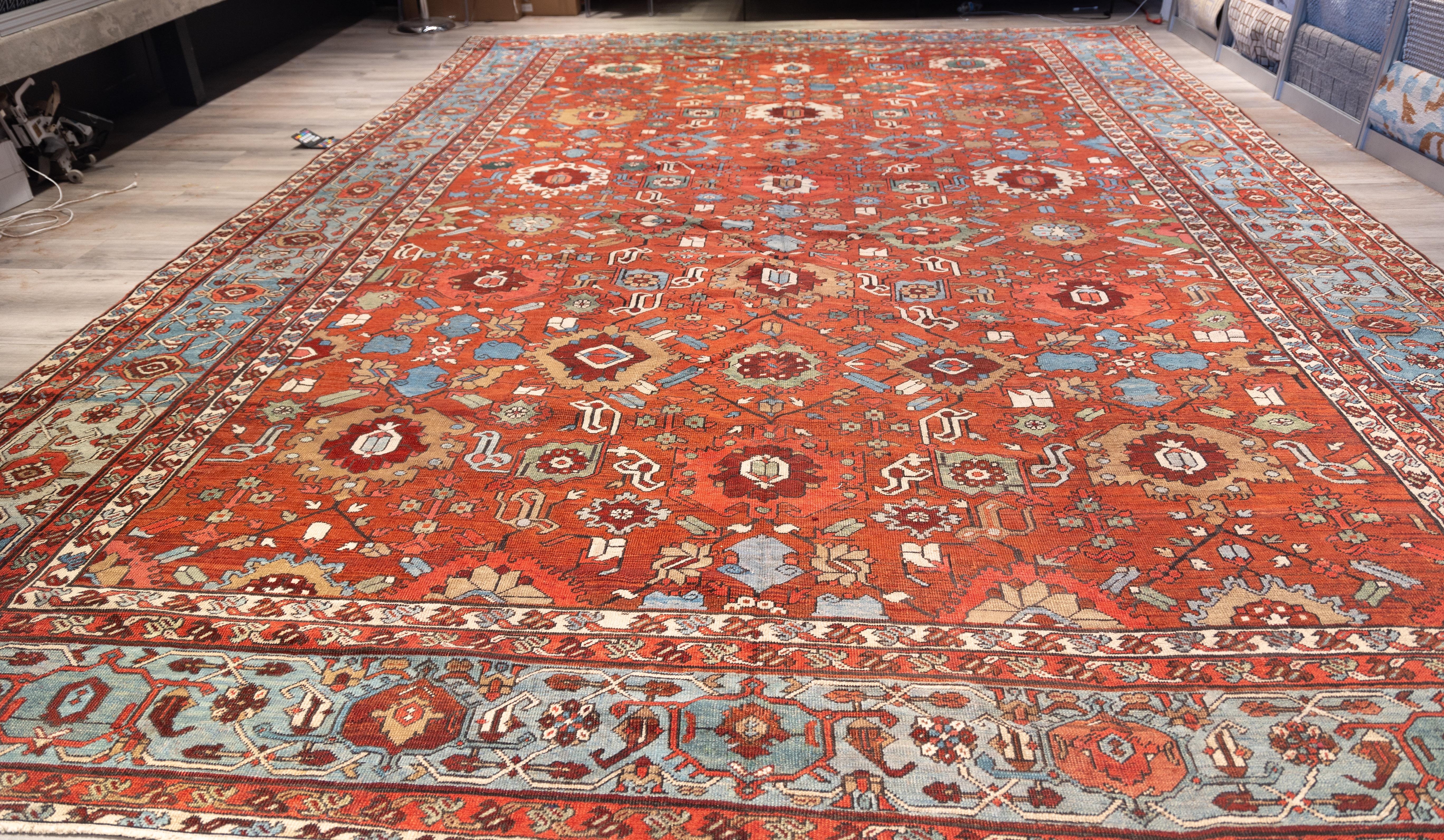 A large  allover design Serapi with stylized geometric floral forms distributed across a rich brick-red field. The primary motifs include angular rosettes, serrated palmettes, and hooked medallions, arranged in a staggered layout that creates a
