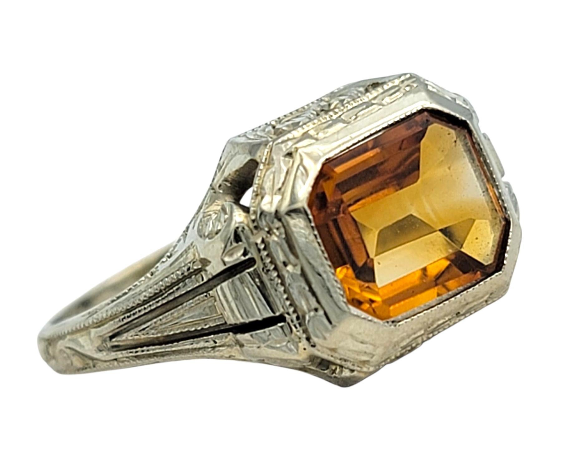 Cette bague ancienne de Charme Antiques met en valeur une citrine orange de taille émeraude, qui brille d'un éclat chaleureux et d'un charme vintage. Sertie en or blanc 20 carats, la monture épurée et structurée met en valeur les lignes nettes de la