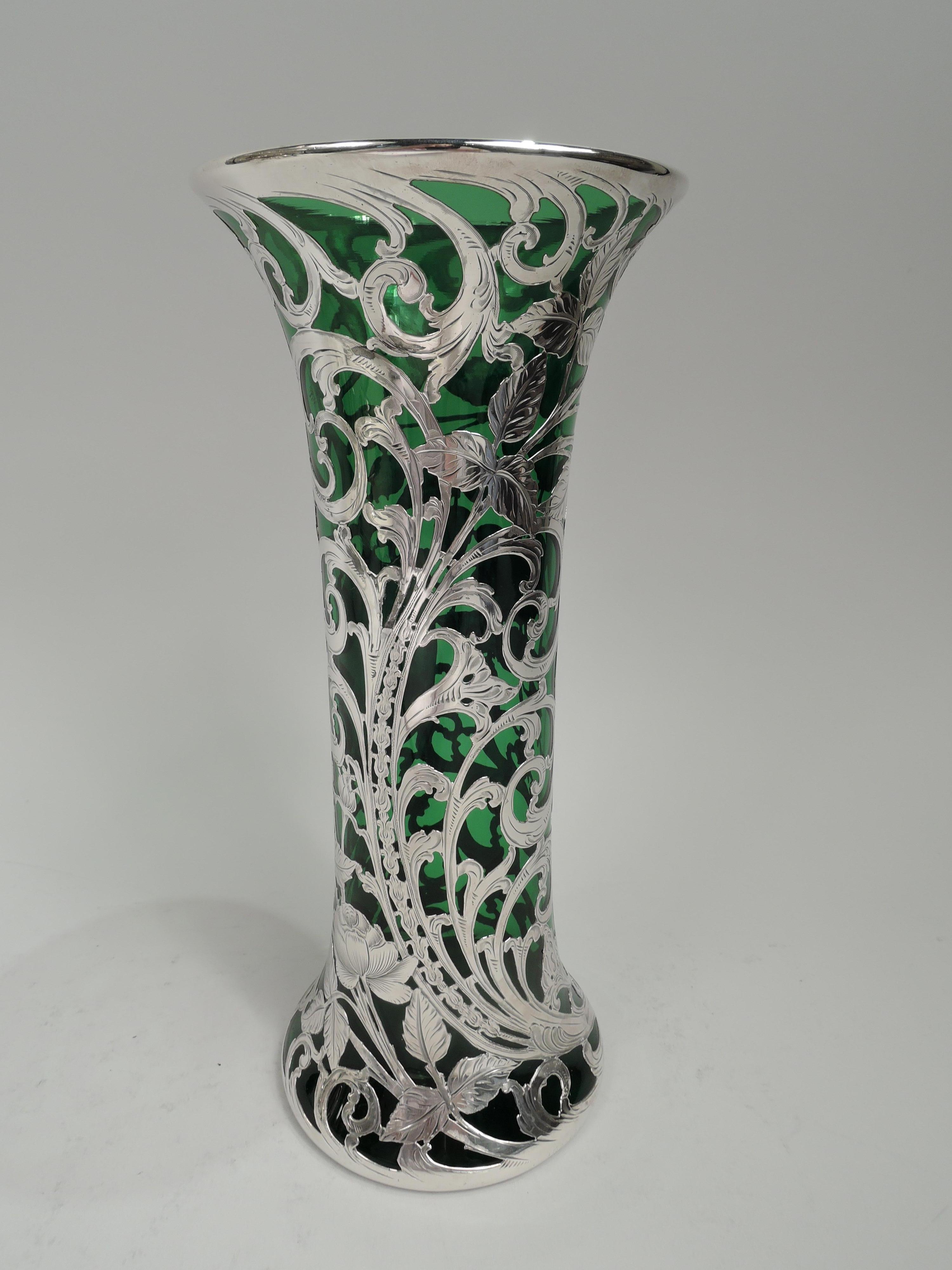 Turn-of-the-century American Art Nouveau glass vase with engraved silver overlay. Cylindrical with flared mouth and spread bae. Dense and scrolling overlay in form of leafing and flowering tendrils, and scrolled cartouche (vacant). Glass is green.