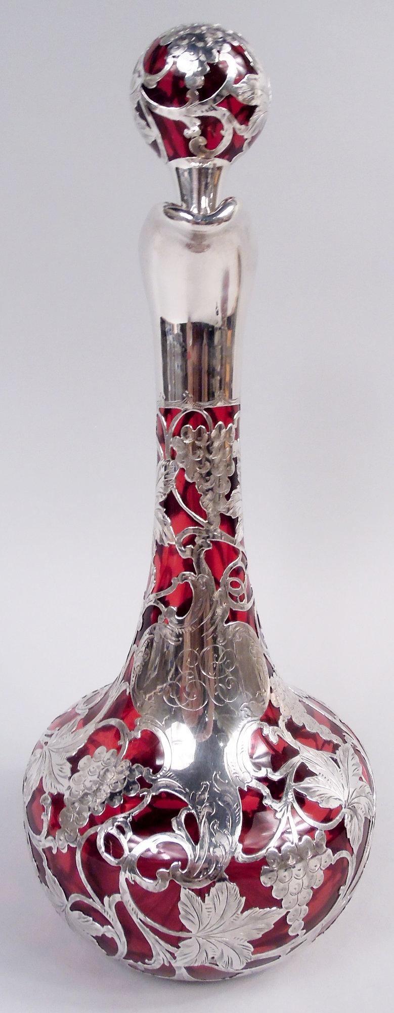 Art Nouveau glass decanter with engraved silver overlay, ca 1900. Globular bowl and tall cylindrical neck with helmet mouth and high-looping handle in silver collars; ball stopper with shaded plug. Star cut to underside. Fruiting grapevine silver