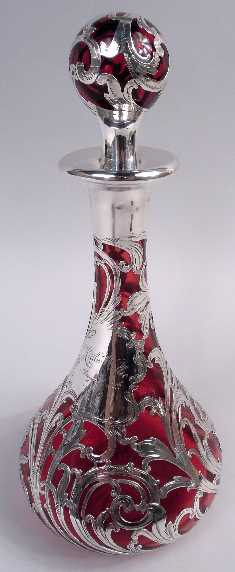 Carafe en verre Art nouveau avec revêtement en argent gravé, vers 1900. Coupe conique avec col cylindrique et bord évasé, collier en argent ; bouchon à bille. Coupure en étoile sur la face inférieure. Motif d'argent à enroulement dynamique ;