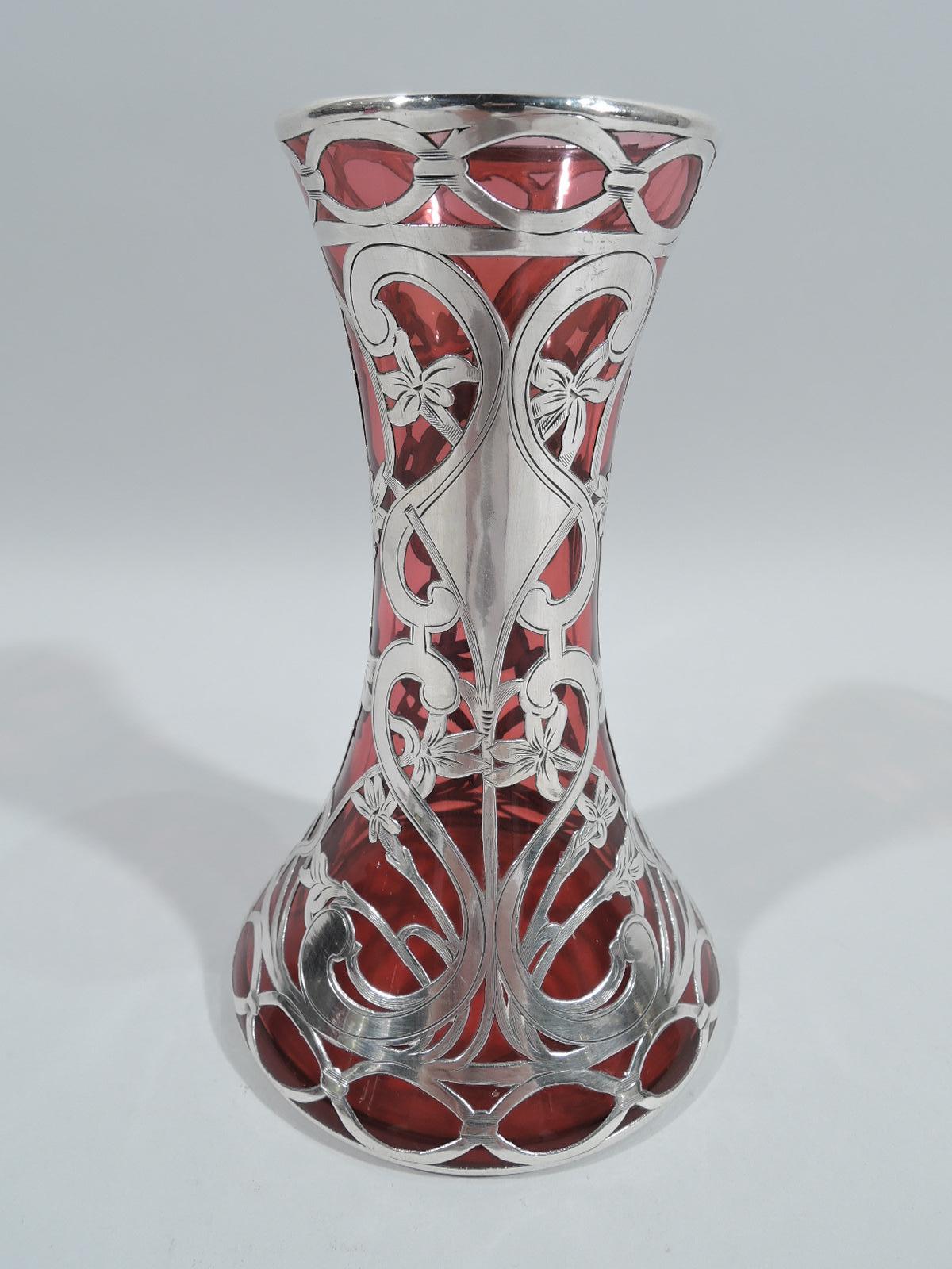 Turn-of-the-century Art Nouveau glass vase with engraved silver overlay. Made by Alvin in Providence. Conical with flared mouth. Overlay comprises s-scrolls entwined with flowering tendrils, and guilloche border at top and bottom. Glass is red.