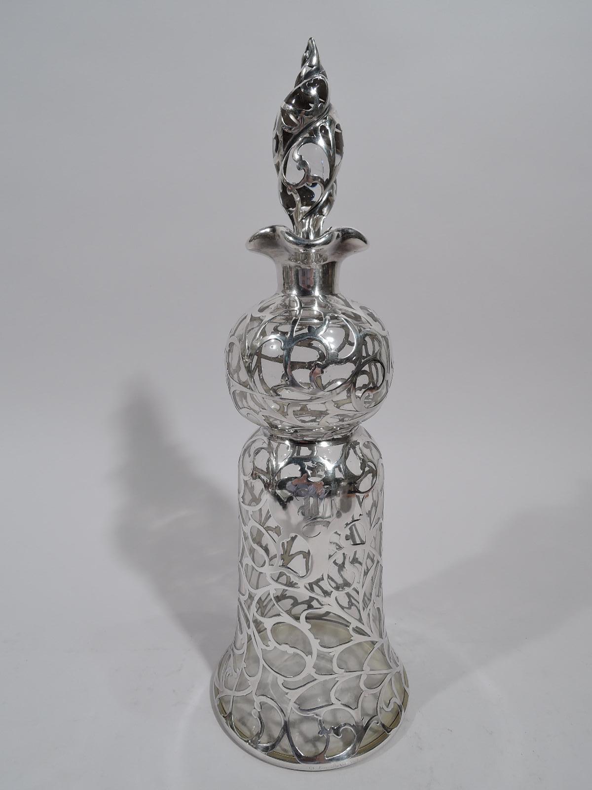 Turn-of-the-century Art Nouveau glass decanter with silver overlay. Globular top and bell-form bottom. Short neck and ruffled quatrefoil mouth in silver collar. Dense scrolling overlay and armorial cartouche engraved with single-letter monogram.