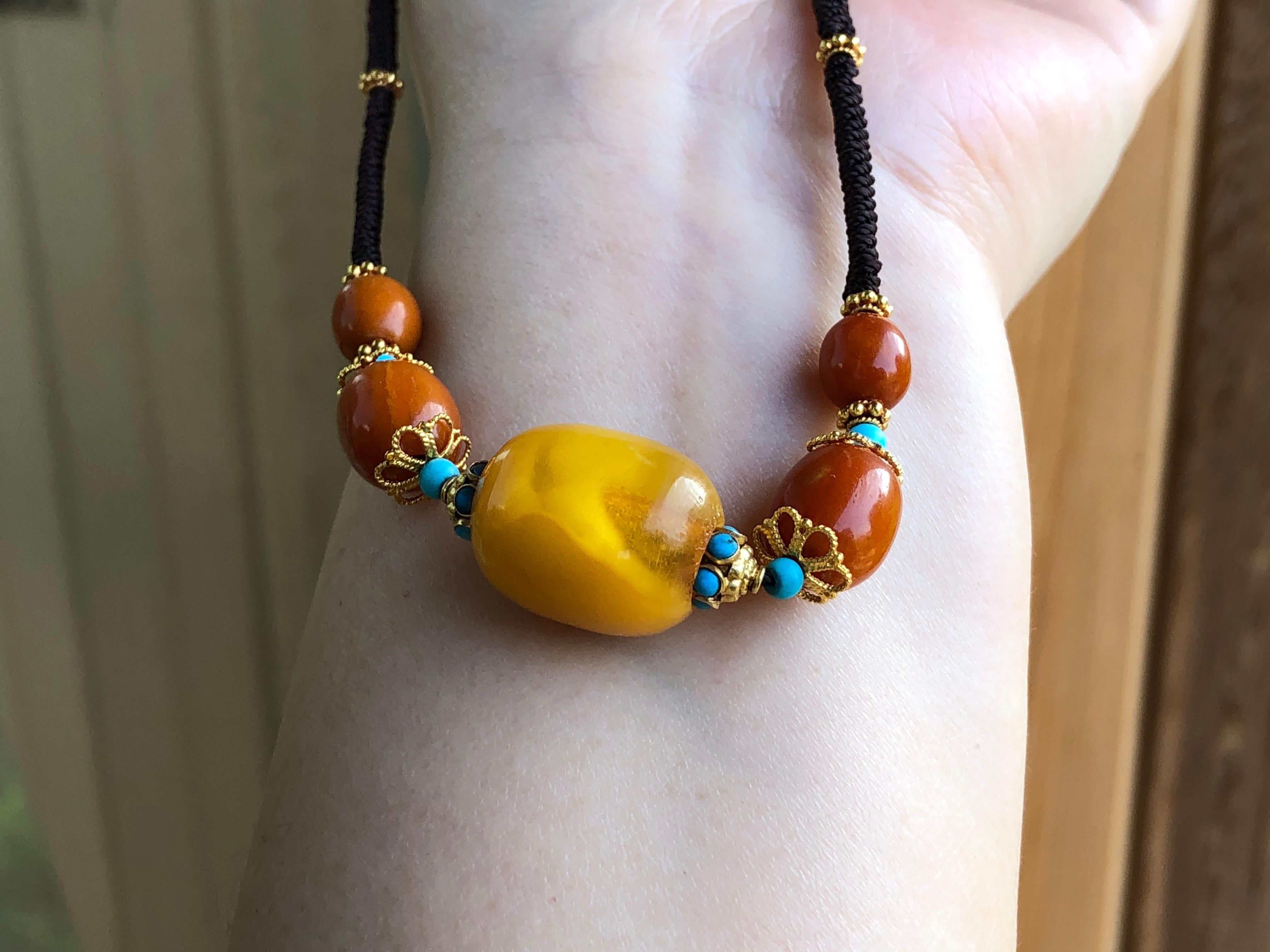 This amber, gold and turquoise necklace is a collection of eye catching contrasts. First there are the colours; the two tones of amber against the black string and the lighter turquoise. Then there is the design. The main focus is the large, bold