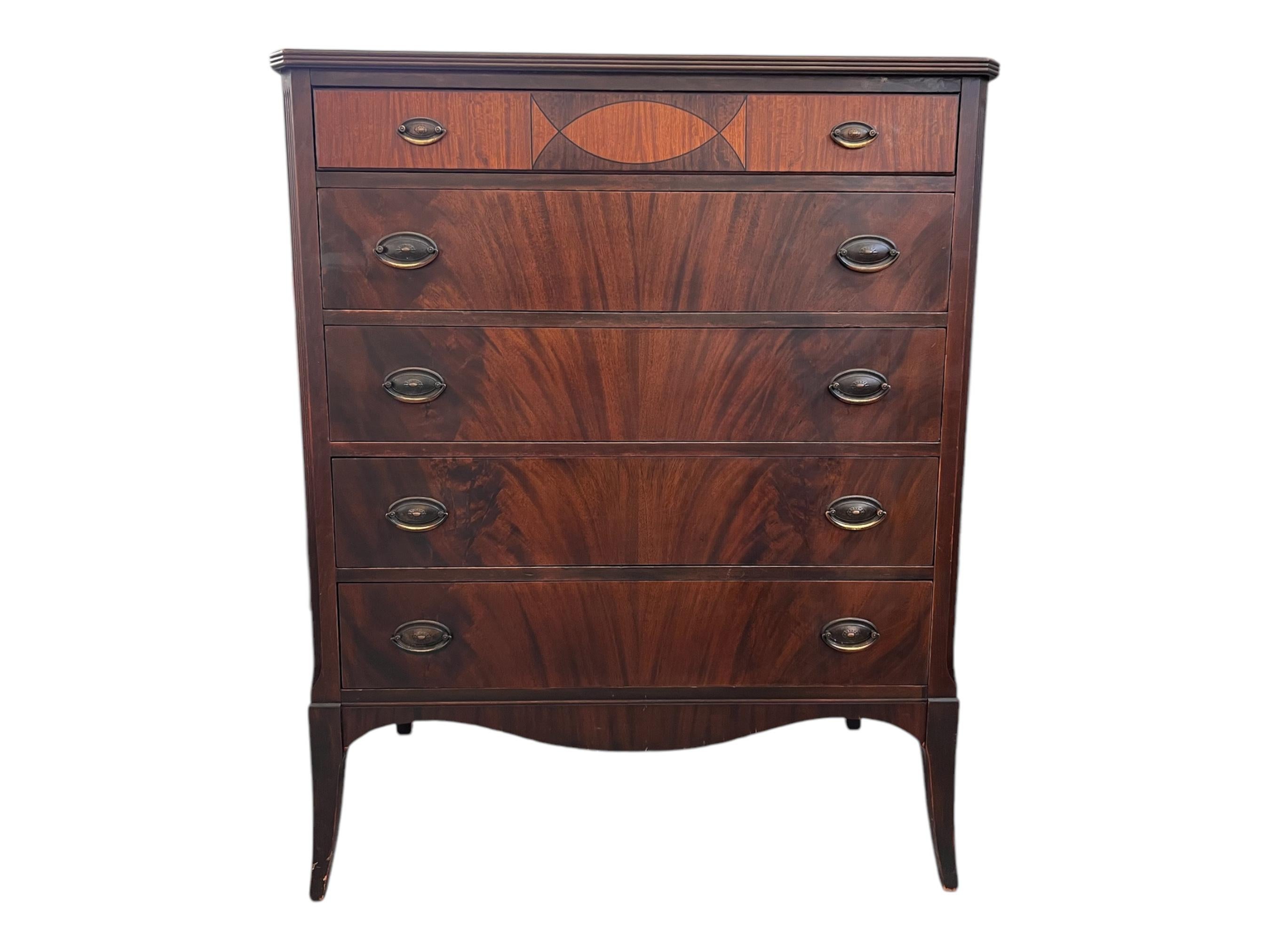 This antique mahogany dresser features a classic design with a warm, rich finish that showcases the natural grain of the wood. It has five drawers, each with flame mahogany fronts and brass finished metal handles, adding a touch of sophistication.