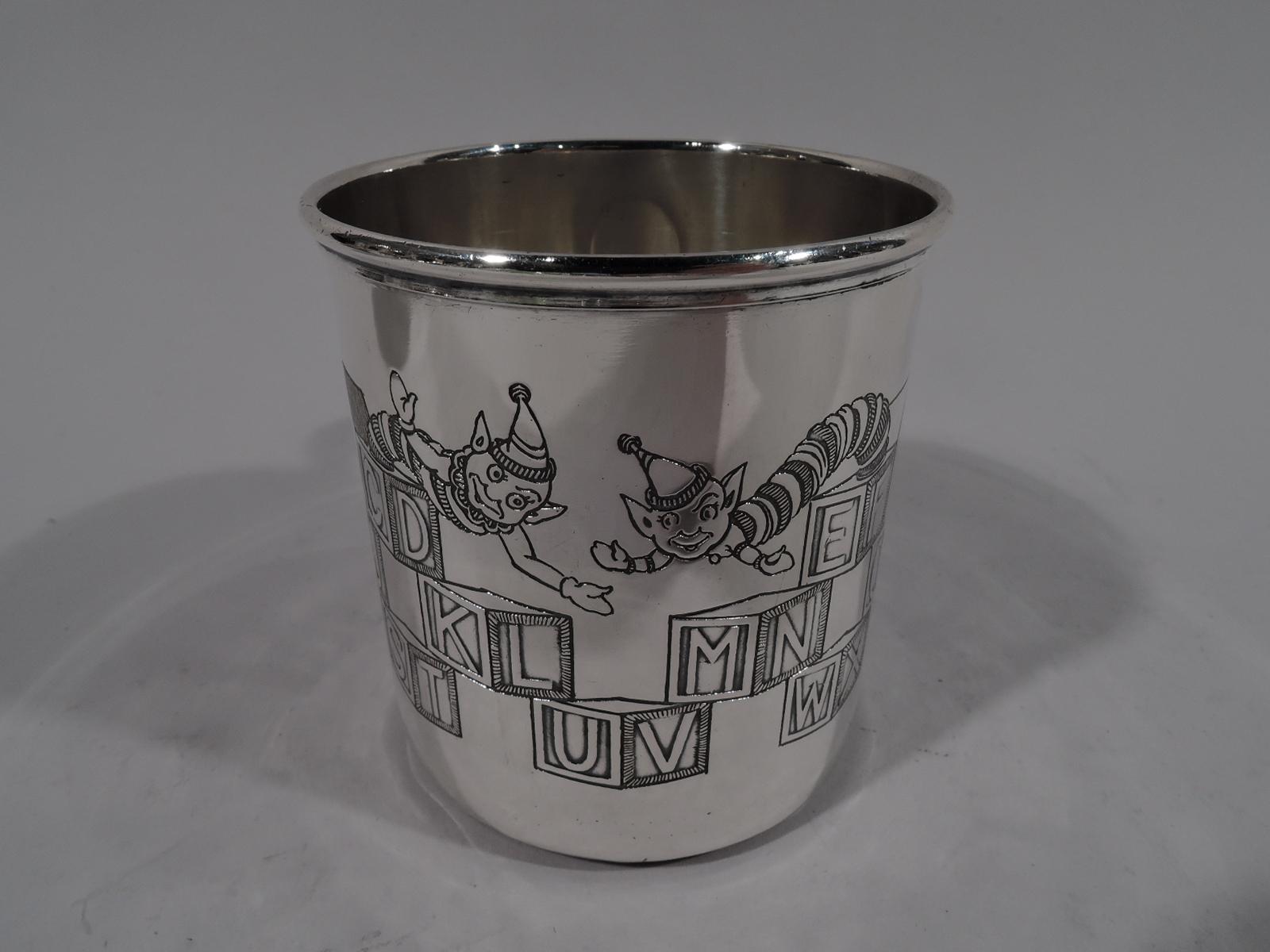 Art Deco sterling silver baby cup. Straight sides and c-scroll handle. On exterior, a girl with ringlets and another with a bob lean against stacks of lettered boxes, some with springing jacks. All letters represented, starting with A for adorable,