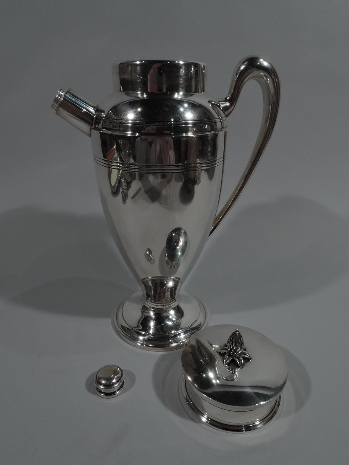 Art Deco sterling silver cocktail shaker. Made by Redlich in New York, ca 1925. Ovoid body, stepped and domed foot, high-looping scroll handle, and straight and stubby spout with built-in strainer and threaded cap. Short neck with flat cover