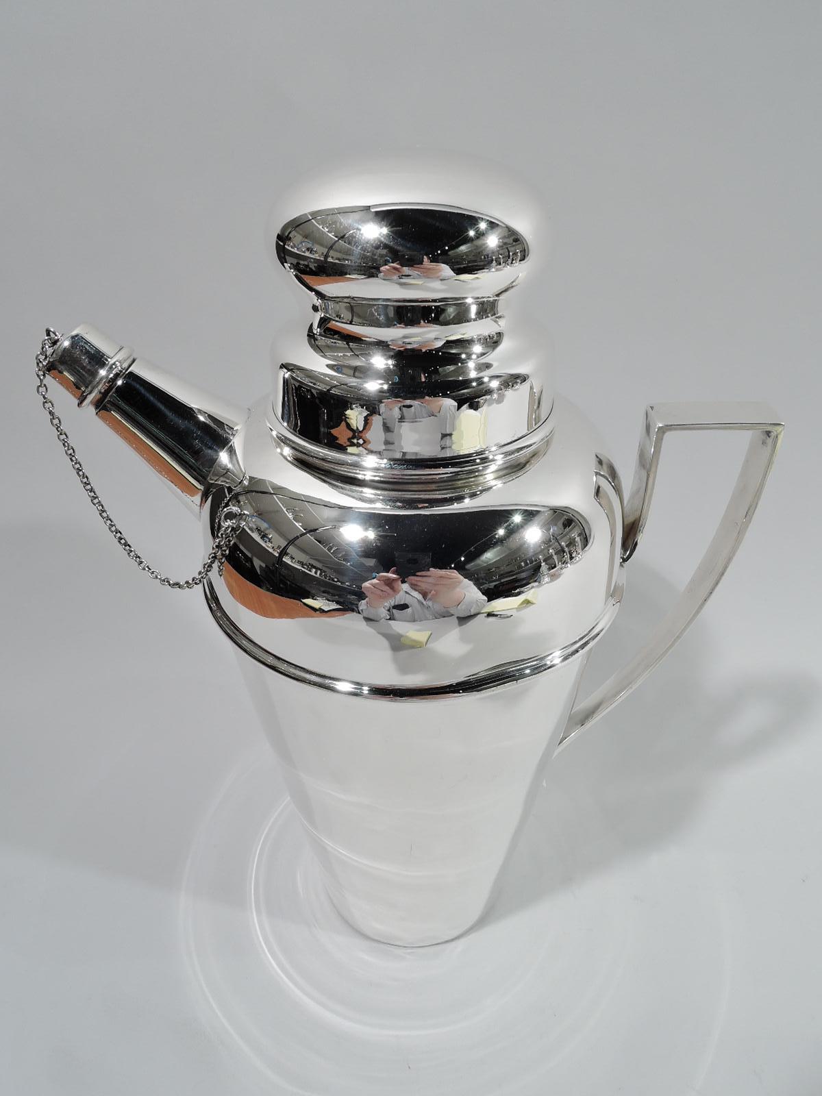 American Art Deco sterling silver cocktail shaker, ca 1925. Straight and tapering bowl with domed top and short neck. Straight and stubby spout with built-in strainer, chained cap, and high-looping handle. Cover snug-fitting with round easy-grip