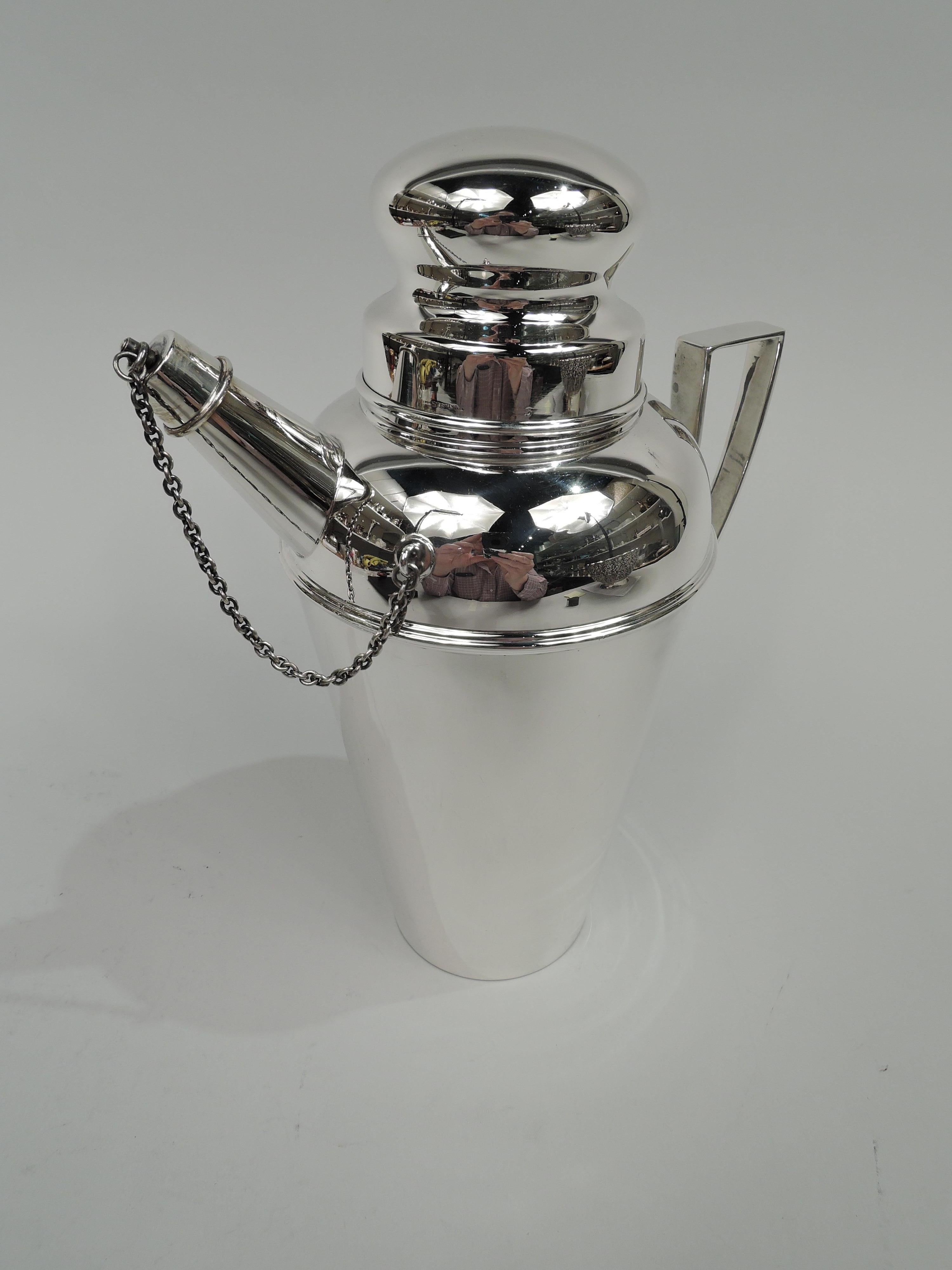 Art Deco sterling silver cocktail shaker, circa 1920. Straight and tapering bowl with curved shoulder, scroll bracket handle, and stubby diagonal spout with threaded chained cap. Inset neck with snug-fitting bun cover. Fully marked including maker’s