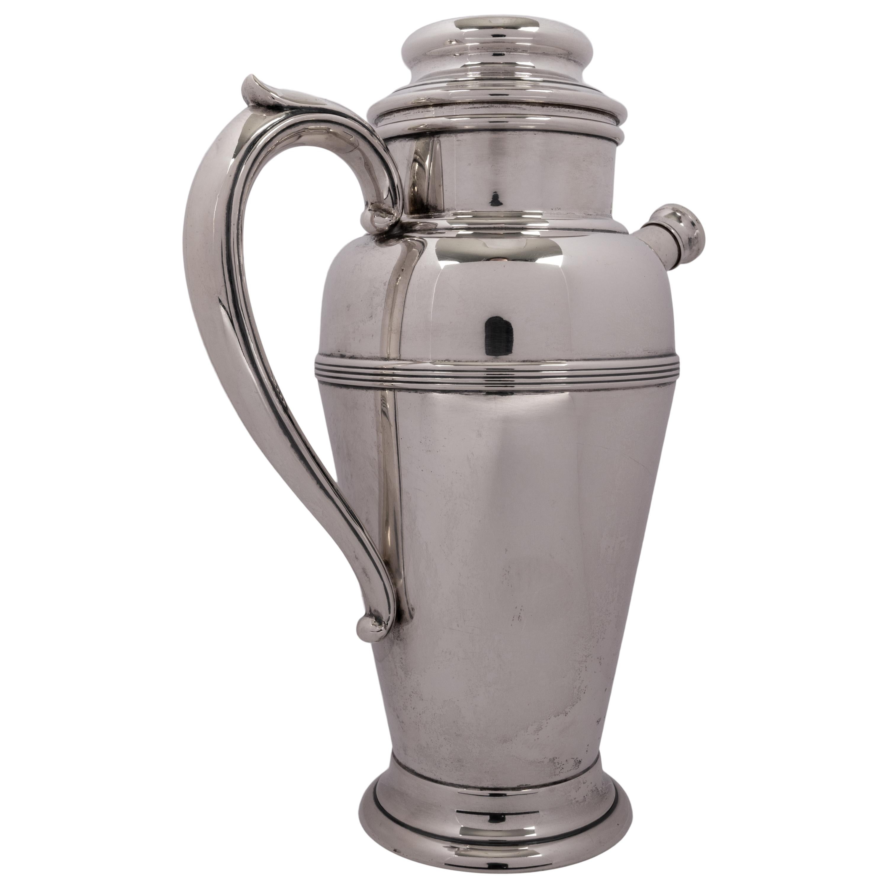 A good antique American Art Deco sterling silver cocktail Shaker and pitcher, by Fisher Silversmiths of New York, circa 1930.
The Shaker having a rounded lid with a knopped finial, to the side is a deeply flared handle exhibiting the exuberance of