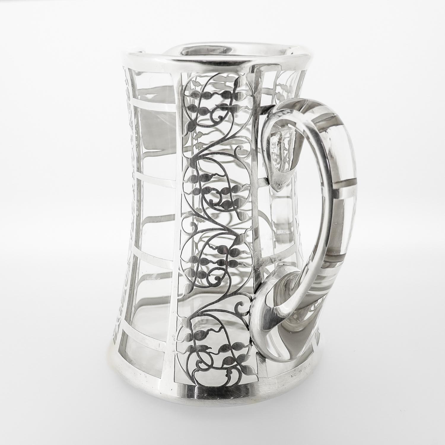 A fine antique Art Deco water or cocktail pitcher.

In blown glass with an applied handle and a thick sterling silver overlay.

With a repeating trellis and stylized vine pattern throughout.

Marked Sterling the foot and with a polished to the
