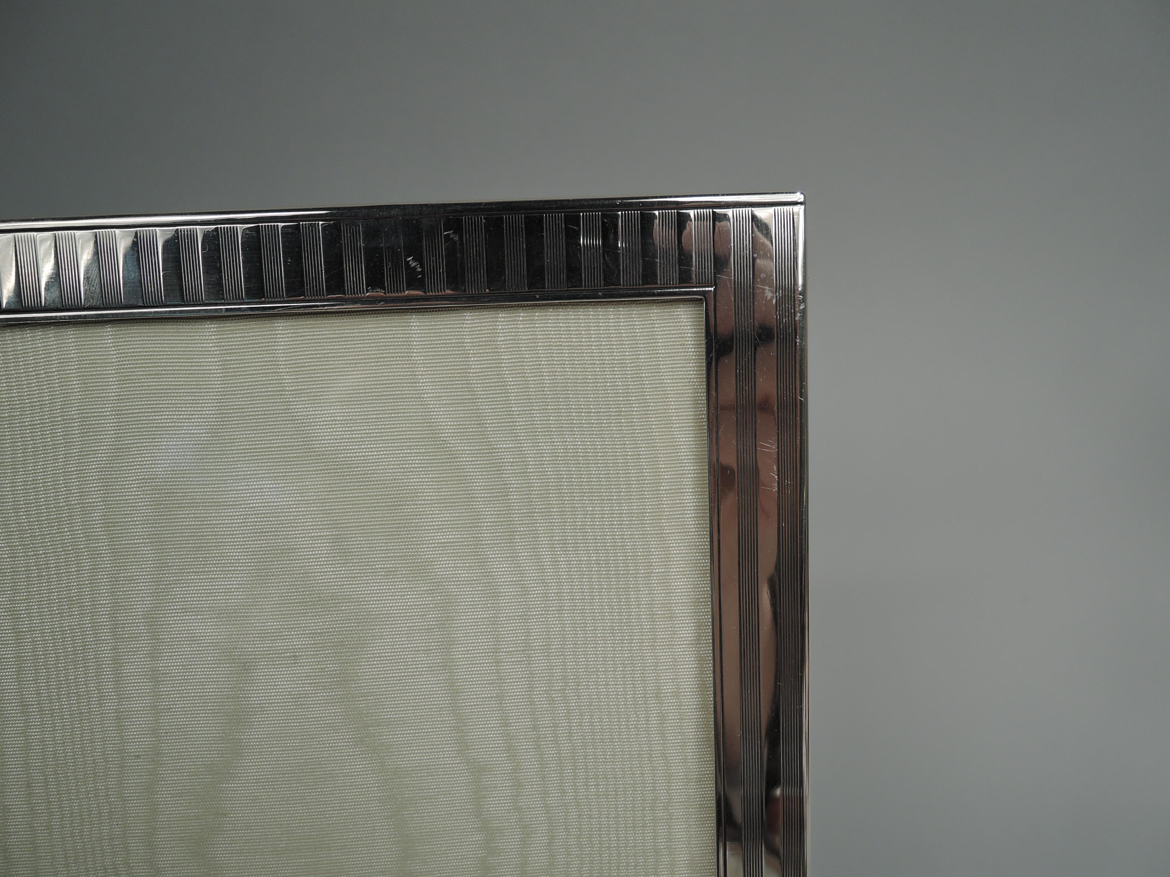 Art Deco sterling silver picture frame with classic linear ornament. Made by JF Fradley & Co. in New York, ca 1920. Rectangular window in same surround with vertical plain and engine-turned through stripes. Bottom rail larger with lozenge mono plate