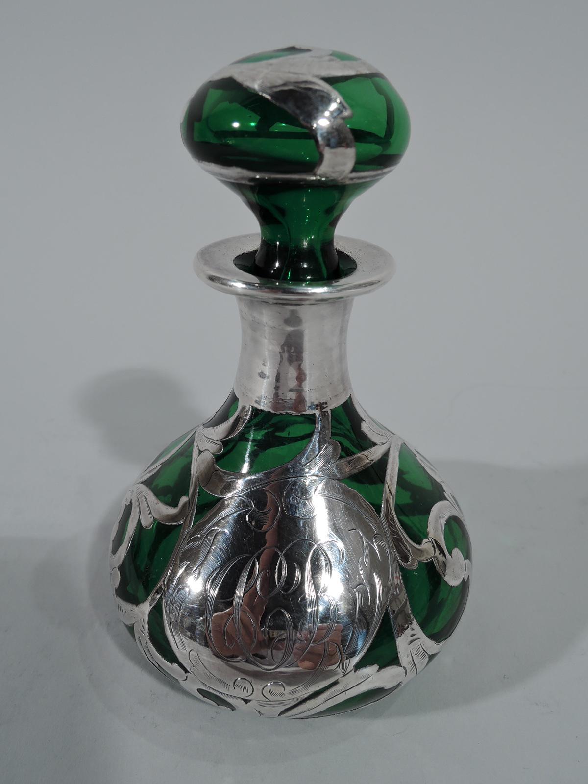 Art Nouveau emerald glass perfume with silver overlay. Bellied bowl and everted rim. Squashed ball stopper with short plug. Engraved overlay in form of scrolled and interlaced tendrils. Scrolled cartouche engraved with script monogram. Faint mark.