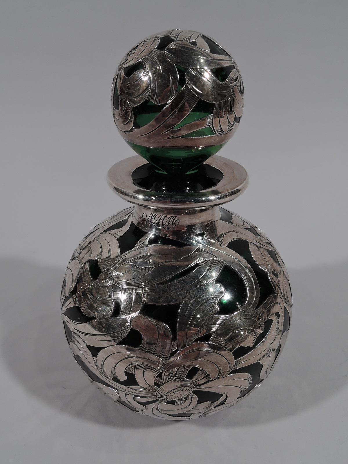 Turn-of-the-century American Art Nouveau green plasss perfume bottle with engraved silver overlay. Globular with short neck and everted rim in collar. Ball stopper. Overlay in dense and dynamic flower head pattern with interlaced and overlapping
