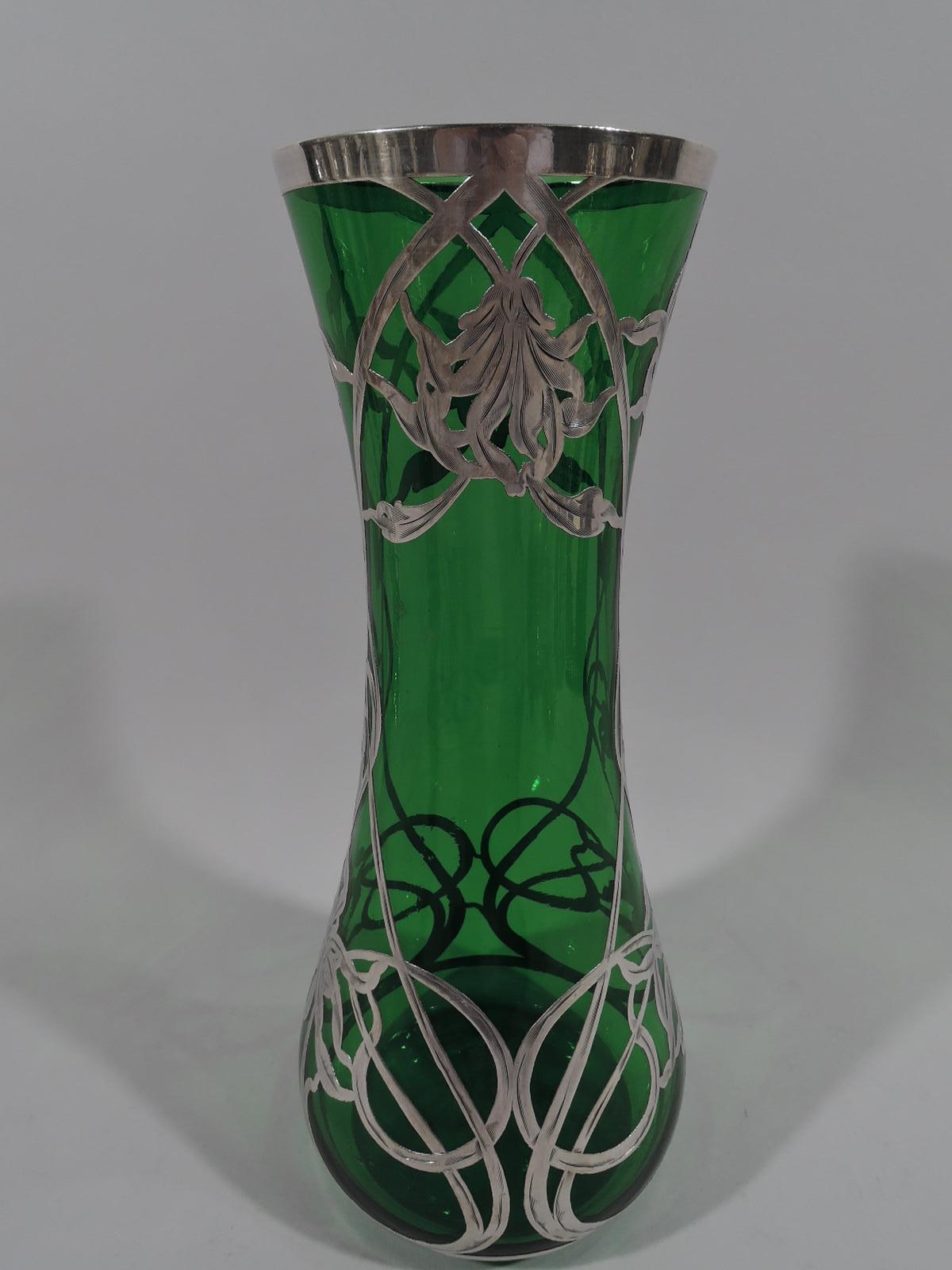 Turn-of-the-century American Art Nouveau green glass vase with engraved silver overlay. Cylindrical with spread bottom. Loose and open overlay with floaty irregular flower heads and interlaced whiplash tendrils.
