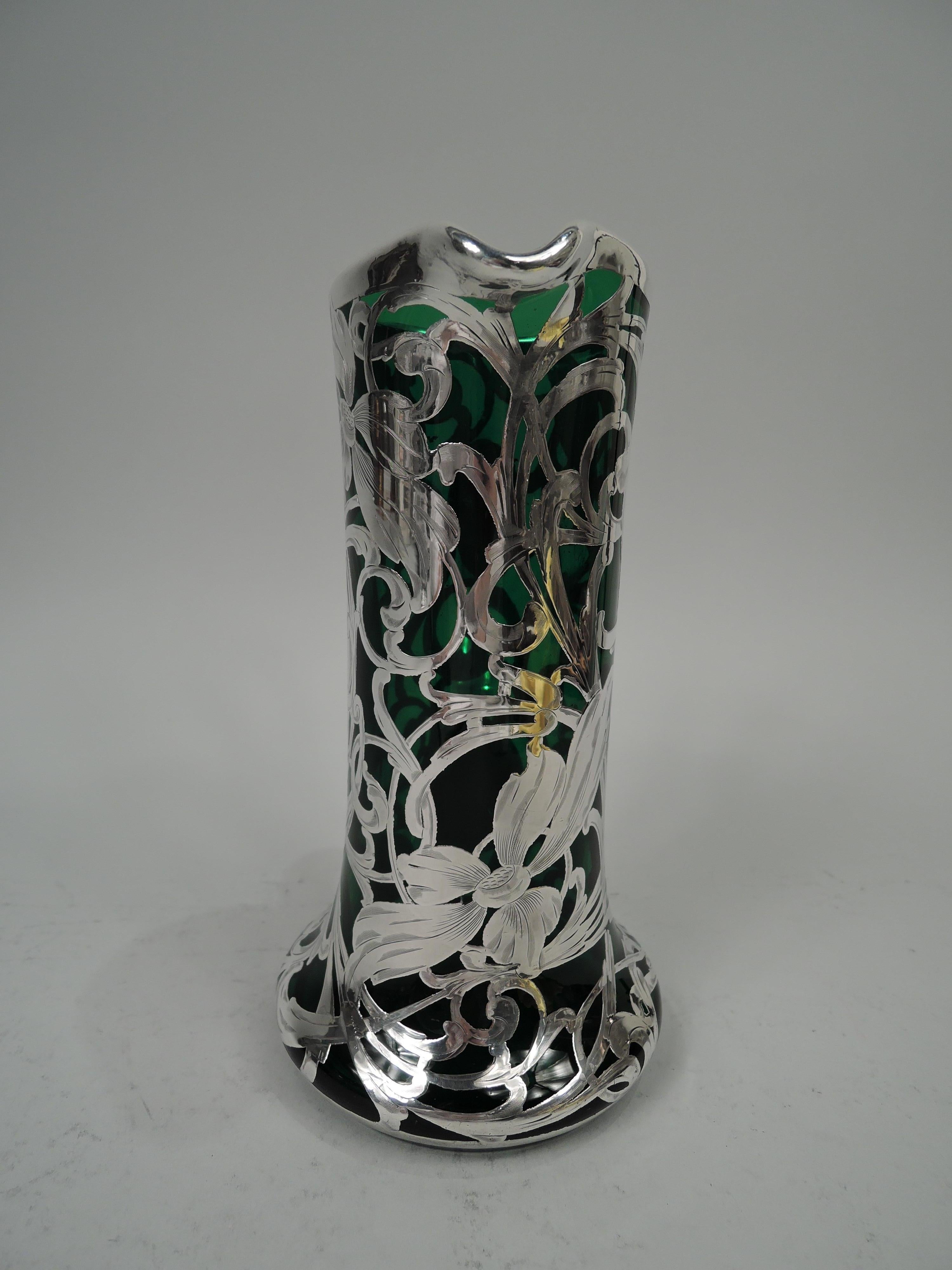 American Art Nouveau glass claret jug with engraved silver overlay, ca 1900. Cylindrical with small lip spout and spread base. C-scroll handle in silver collar. Overlay in form of entwined and whiplash tendrils with distended and elongated flower
